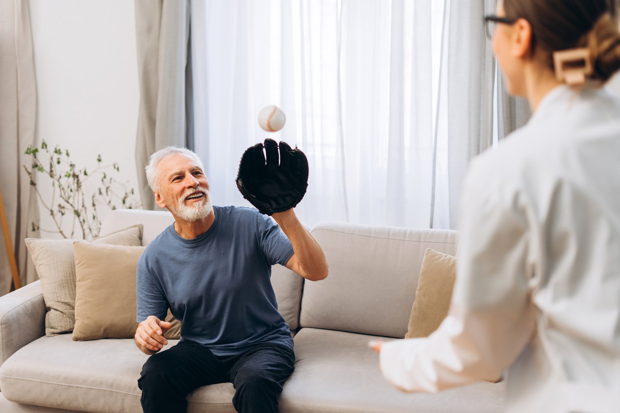 Older man playing catch with a baseball with a woman in a white shirt indoors.