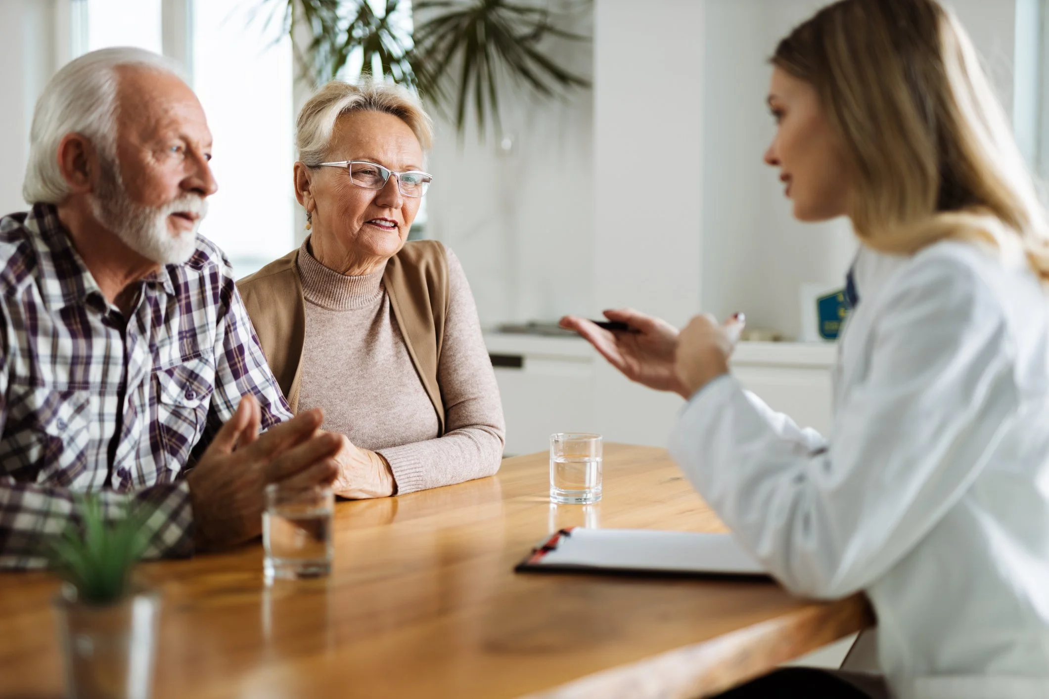 A doctor consulting with an elderly couple in a bright medical office, with glasses and a notepad on the table.