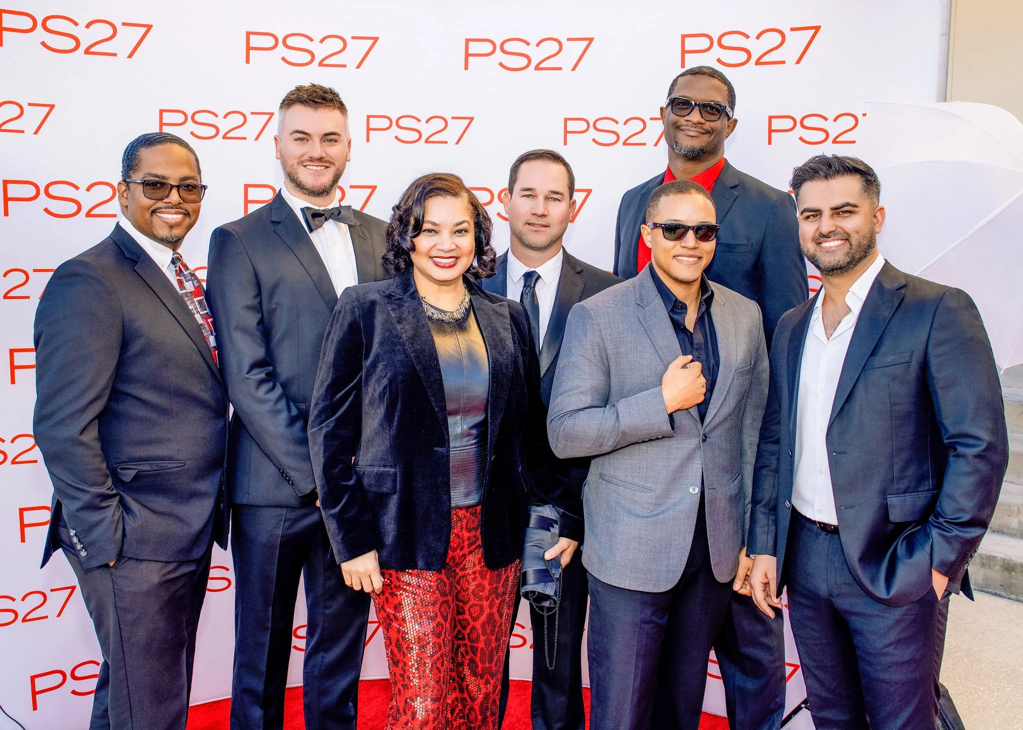 Group of six posing in front of a step and repeat banner at an awards gala