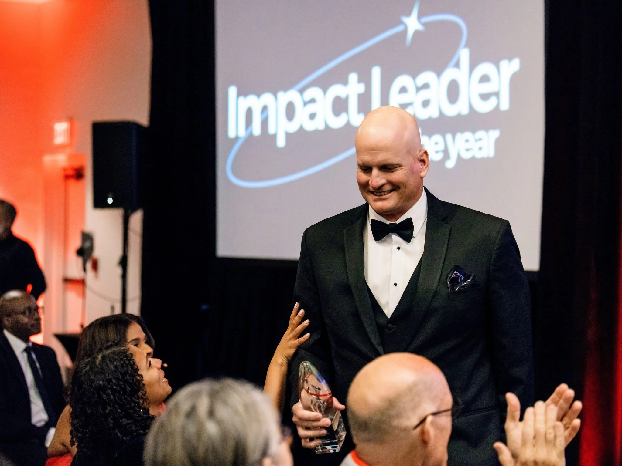 Honoree smiling in front of an Impact Leader of the Year screen at a gala