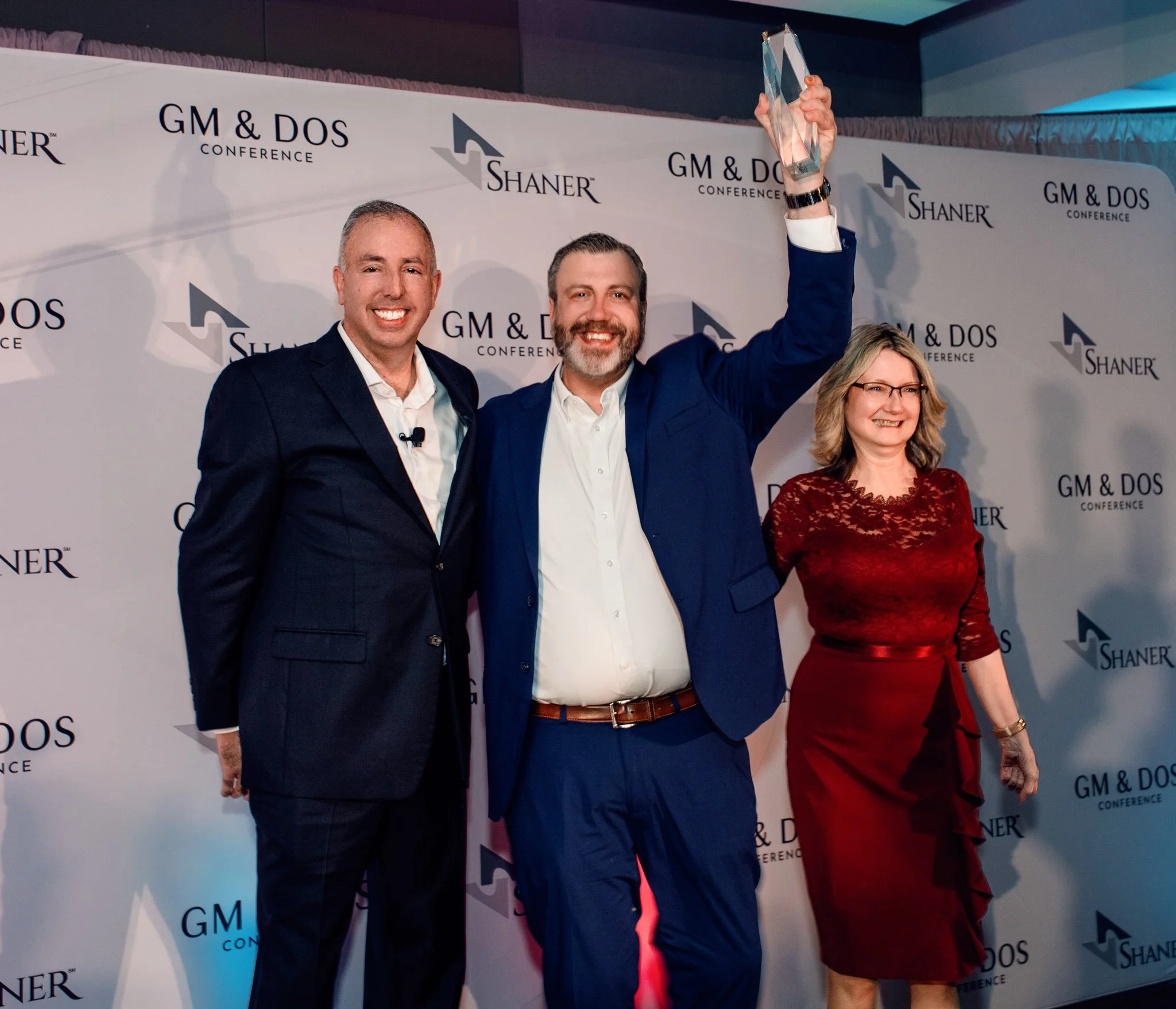 Award winner raising a trophy overhead with two colleagues