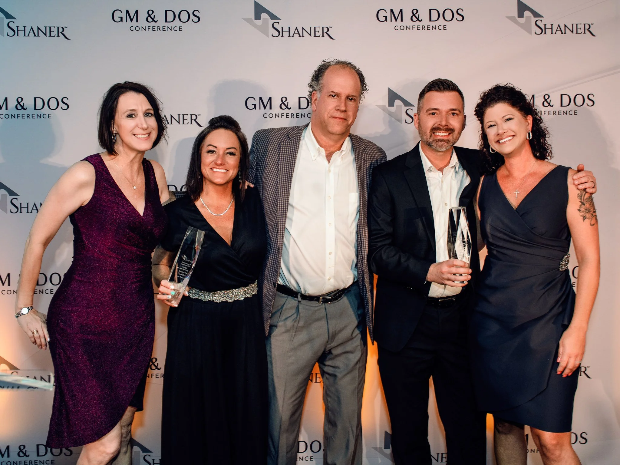Group of five holding awards in front of a sponsor backdrop