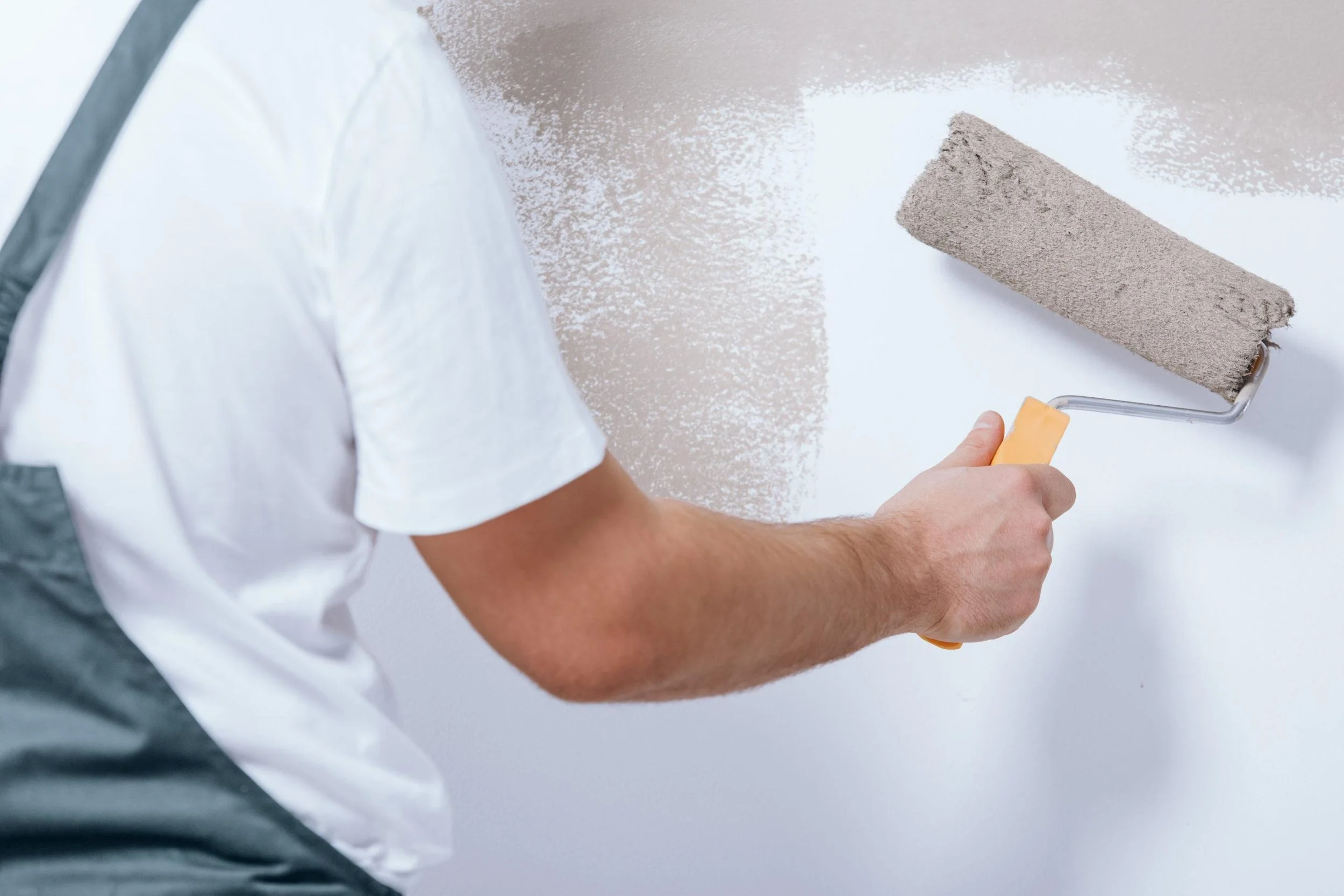 Person painting a wall with a paint roller in white and gray clothing