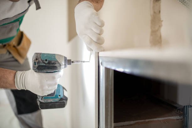 Person wearing gloves using a cordless drill to attach a handle to a cabinet or drawer.