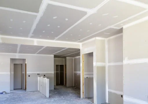 Interior of a house under construction with drywall walls and ceiling, unfinished with visible joints and no paint.