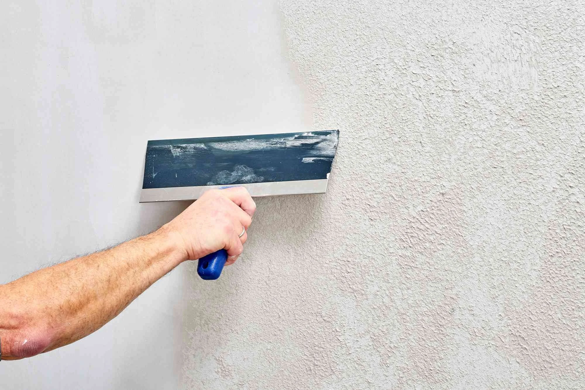 A person smoothing drywall joint compound with a drywall taping knife on a wall.
