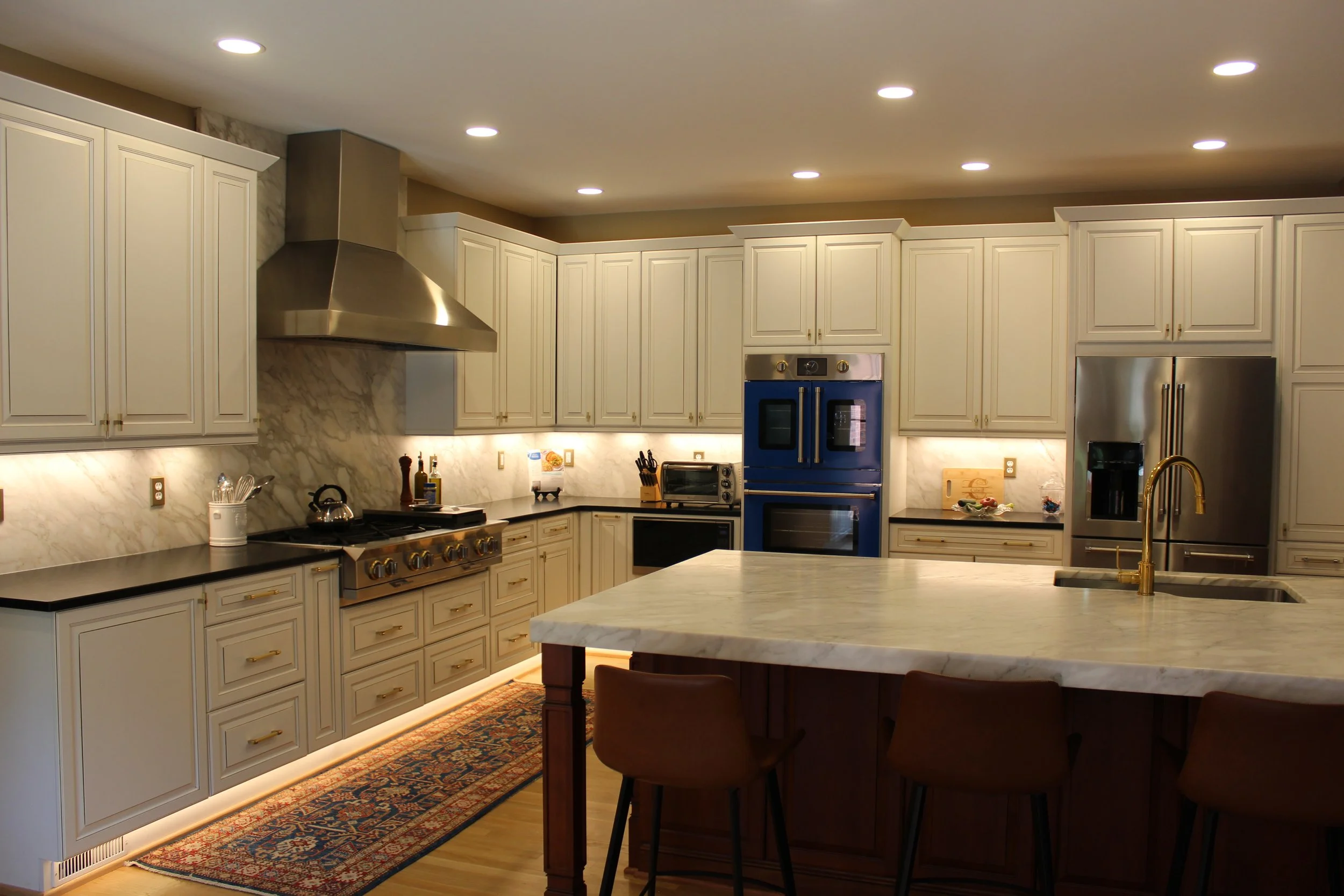Modern kitchen with white cabinetry, marble backsplash, stainless steel appliances, and a marble island with gold faucet.