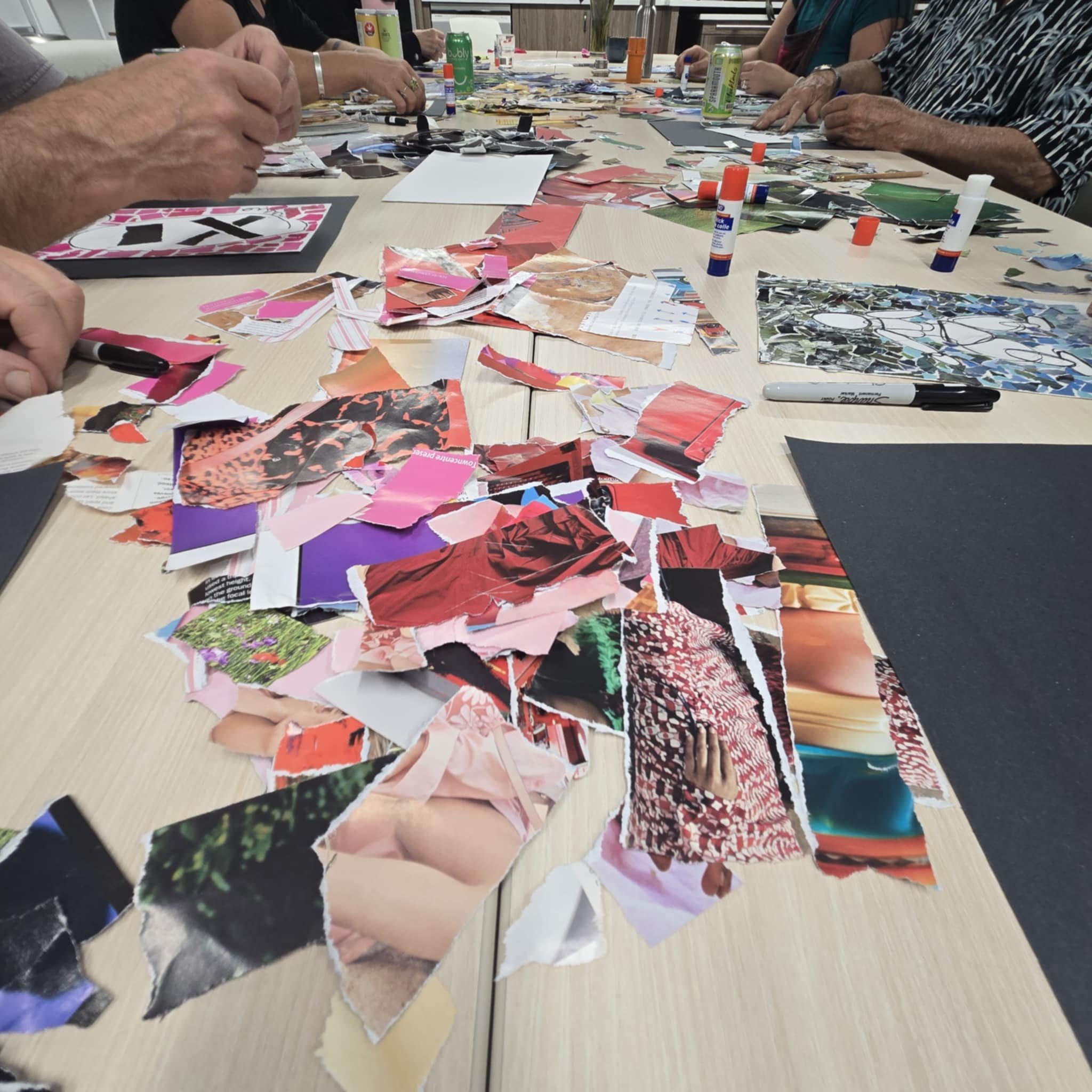 People gathered around a table working on a collage with torn magazine paper and glue sticks.