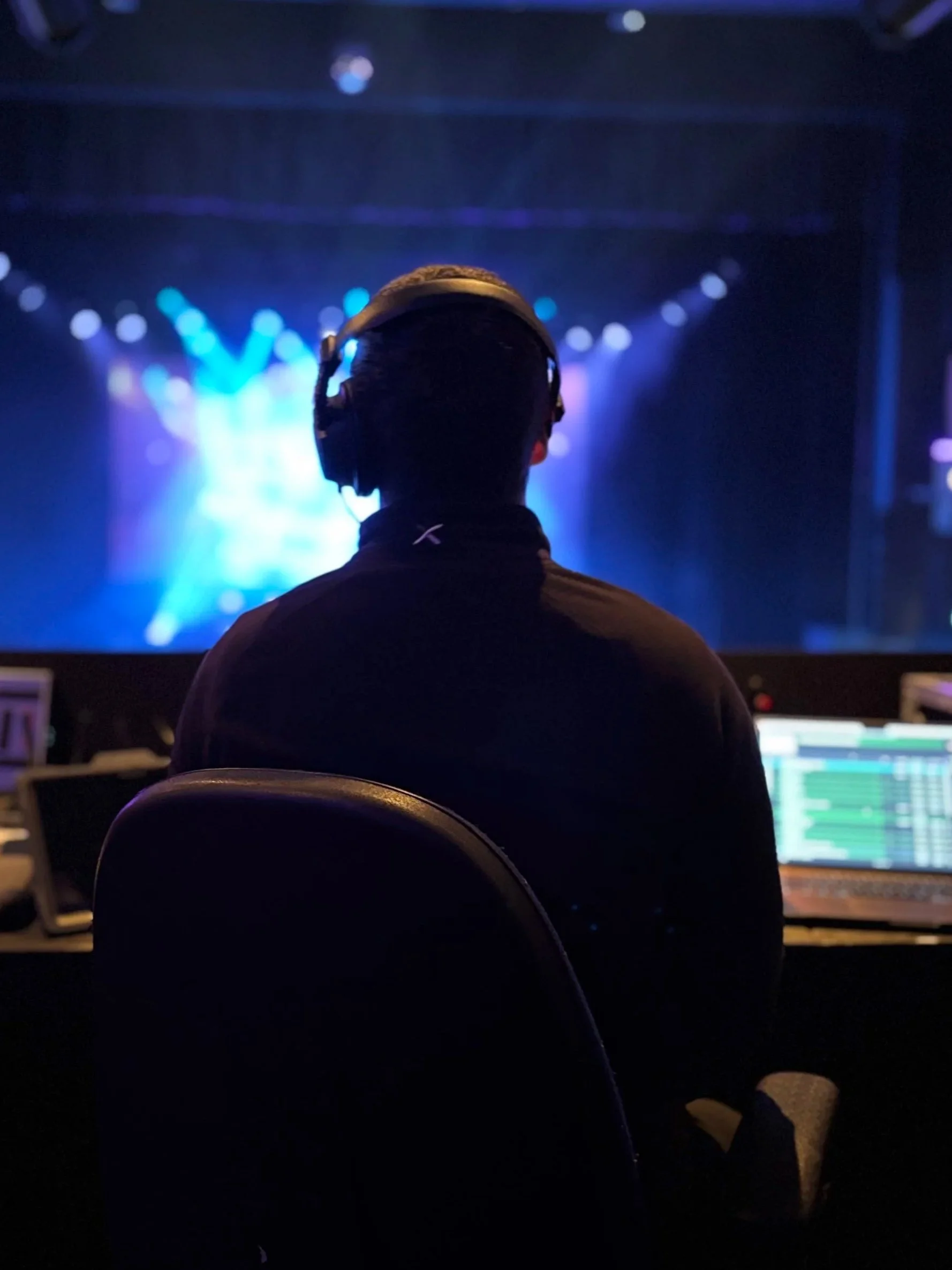 A person wearing headphones sitting in front of a sound mixing console at a music concert