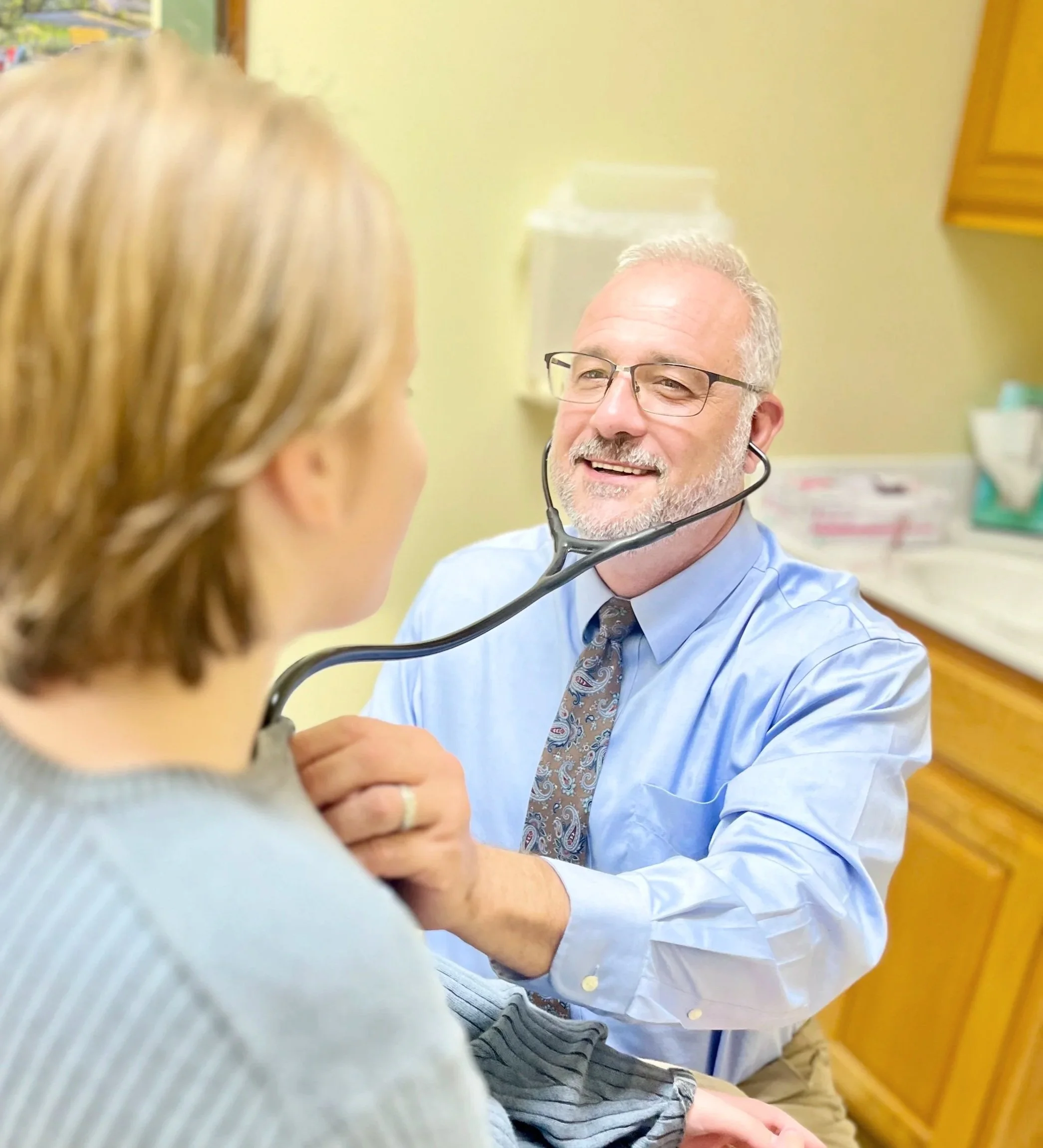 A healthcare provider uses a stethoscope to listen to a patient's chest during a medical examination in a doctor's office.