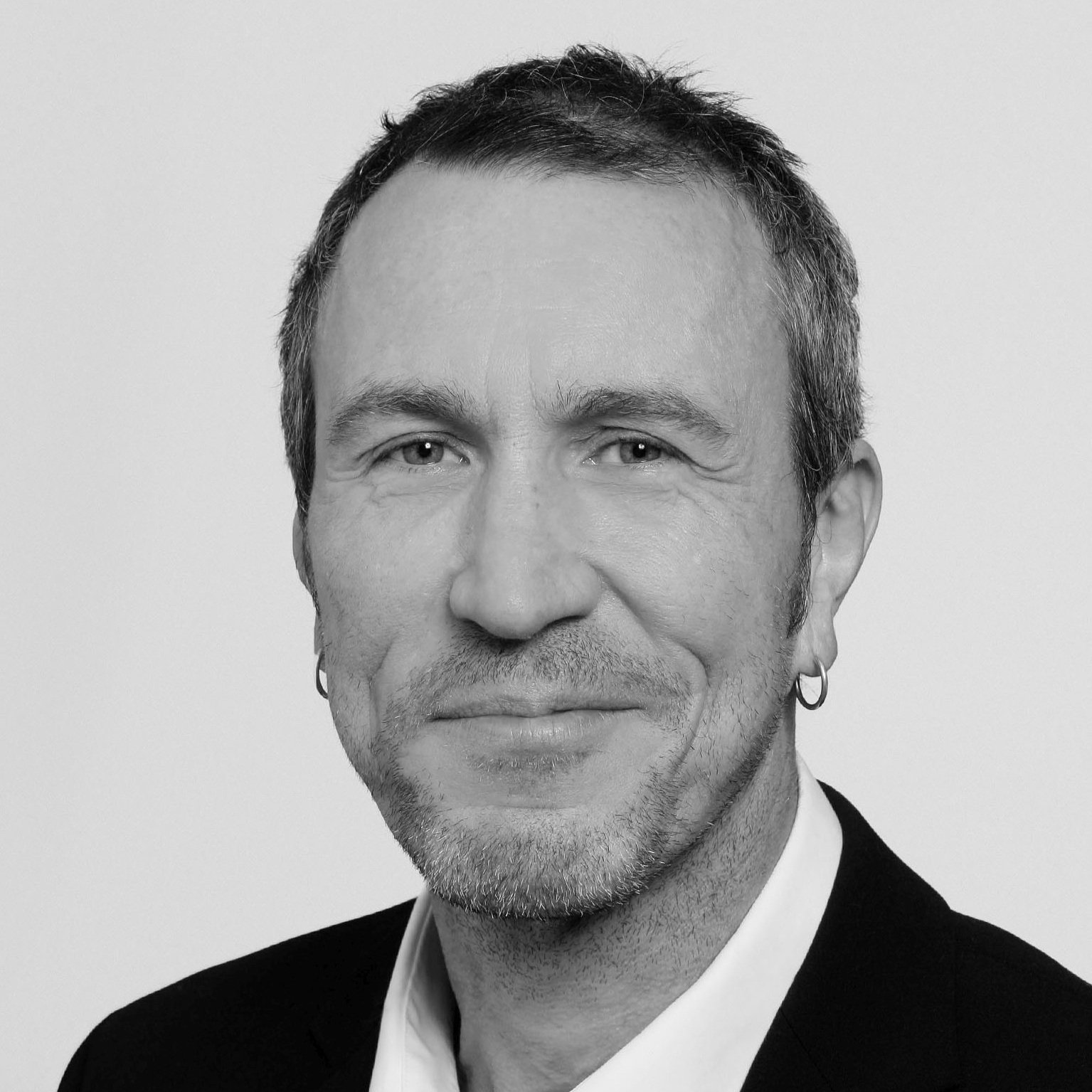 Schwarz-Weiß-Porträt eines Mannes mit kurzen dunklen Haaren, kleinen Ohrringen, Rστcken und einem schwarzen Anzug.