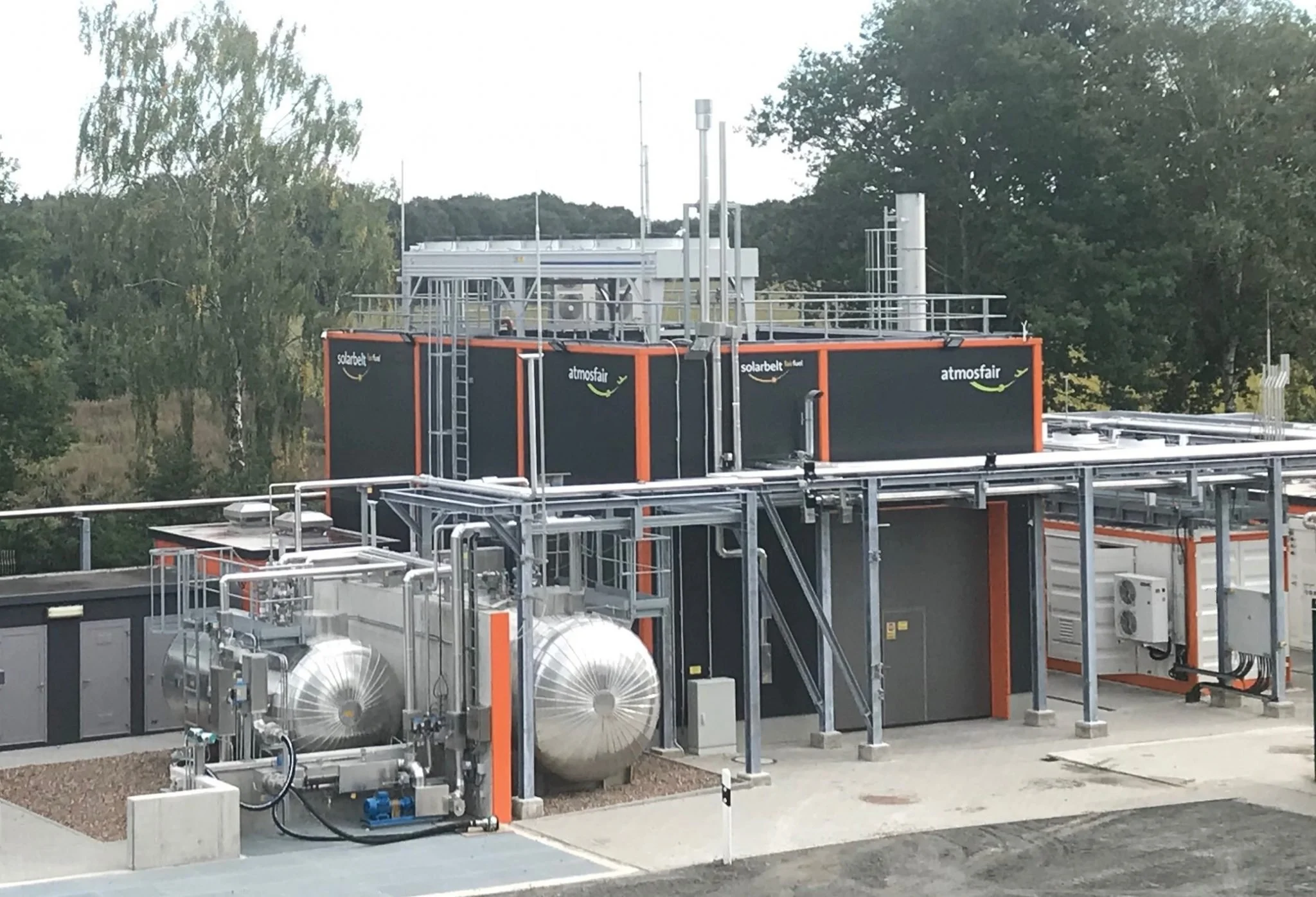 Technische Anlage auf einem Dach mit schwarzen und orangefarbenen Container, Rohren, Tanks und Messgeräten, umweltfreundliche Energielösung