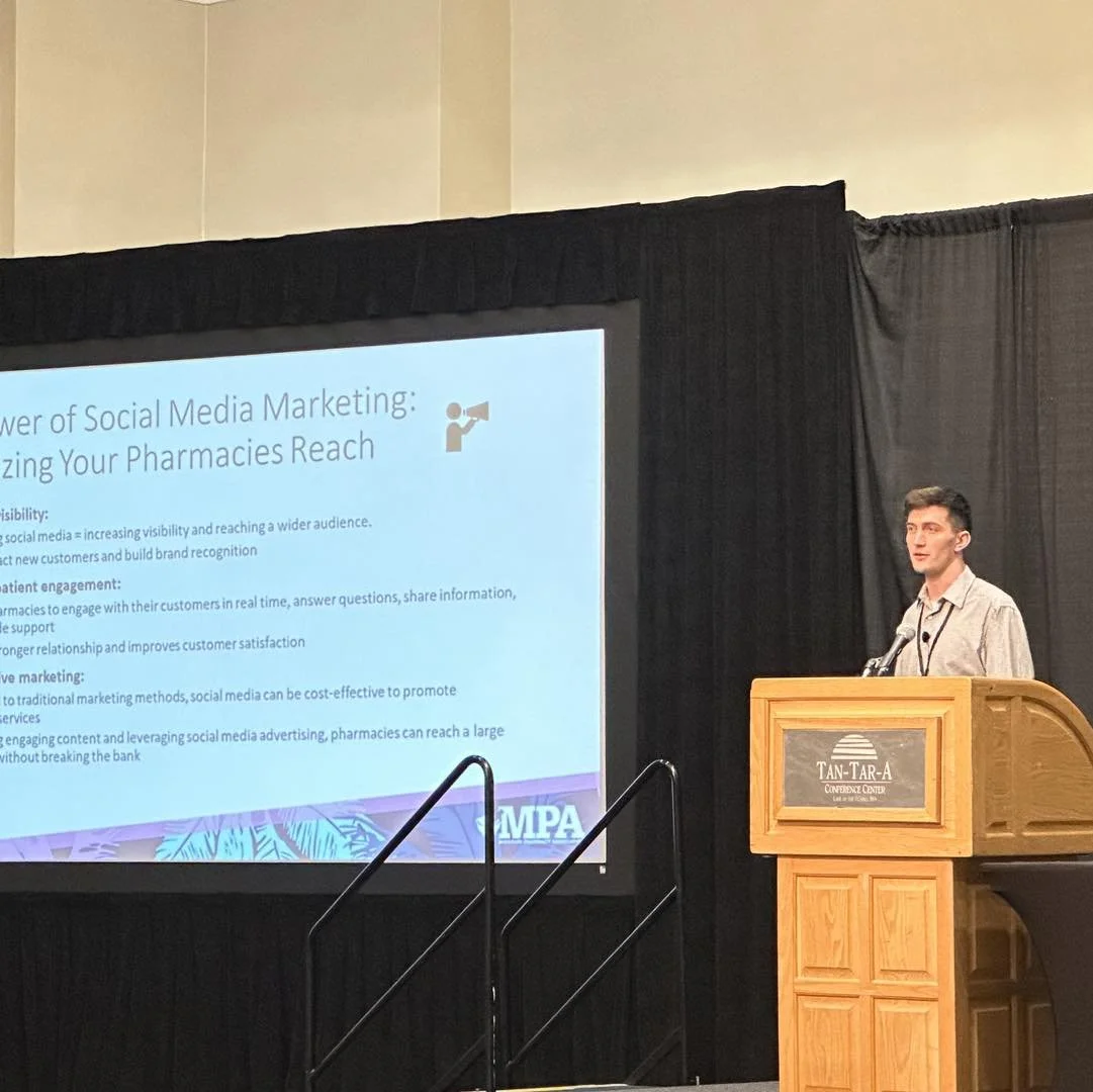 A young man gives a presentation at a podium in front of a large screen at the Tan-Tar-A Conference Center. The slide discusses the power of social media marketing for pharmacies.