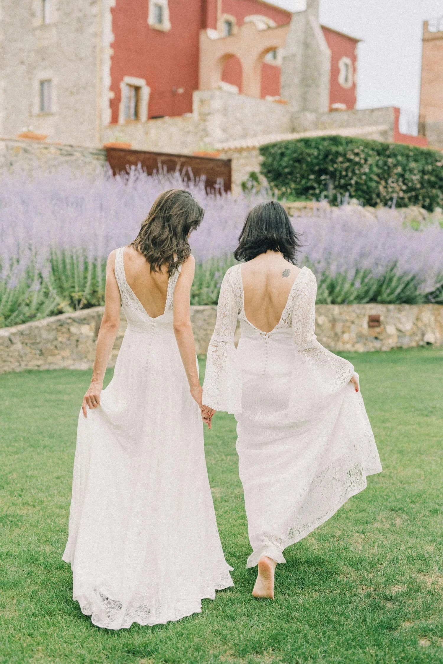 Photo of Two Women in White Wedding Dresses Walking on Grass Field