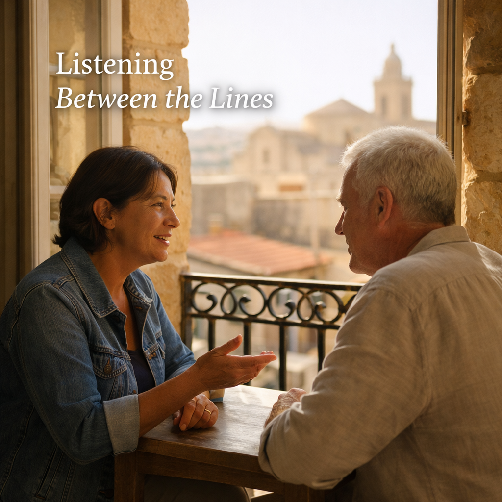 Two people sit near an open stone window in Victoria, Gozo, Malta, engaged in a quiet conversation, with one speaking and the other listening attentively in soft morning light, with the title “Listening Between the Lines” in the upper left.