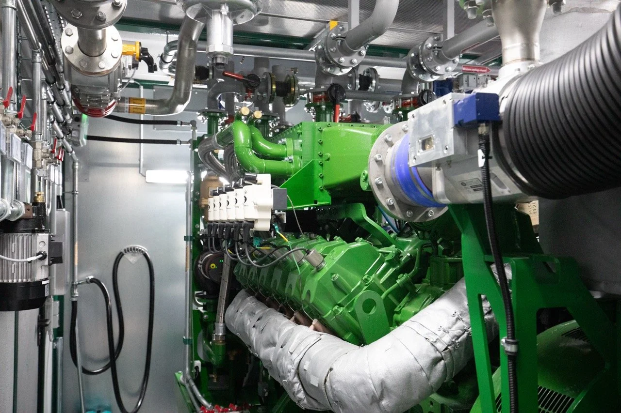 An industrial machine with green, silver, and black components, interconnected pipes, and wiring in a machinery room.