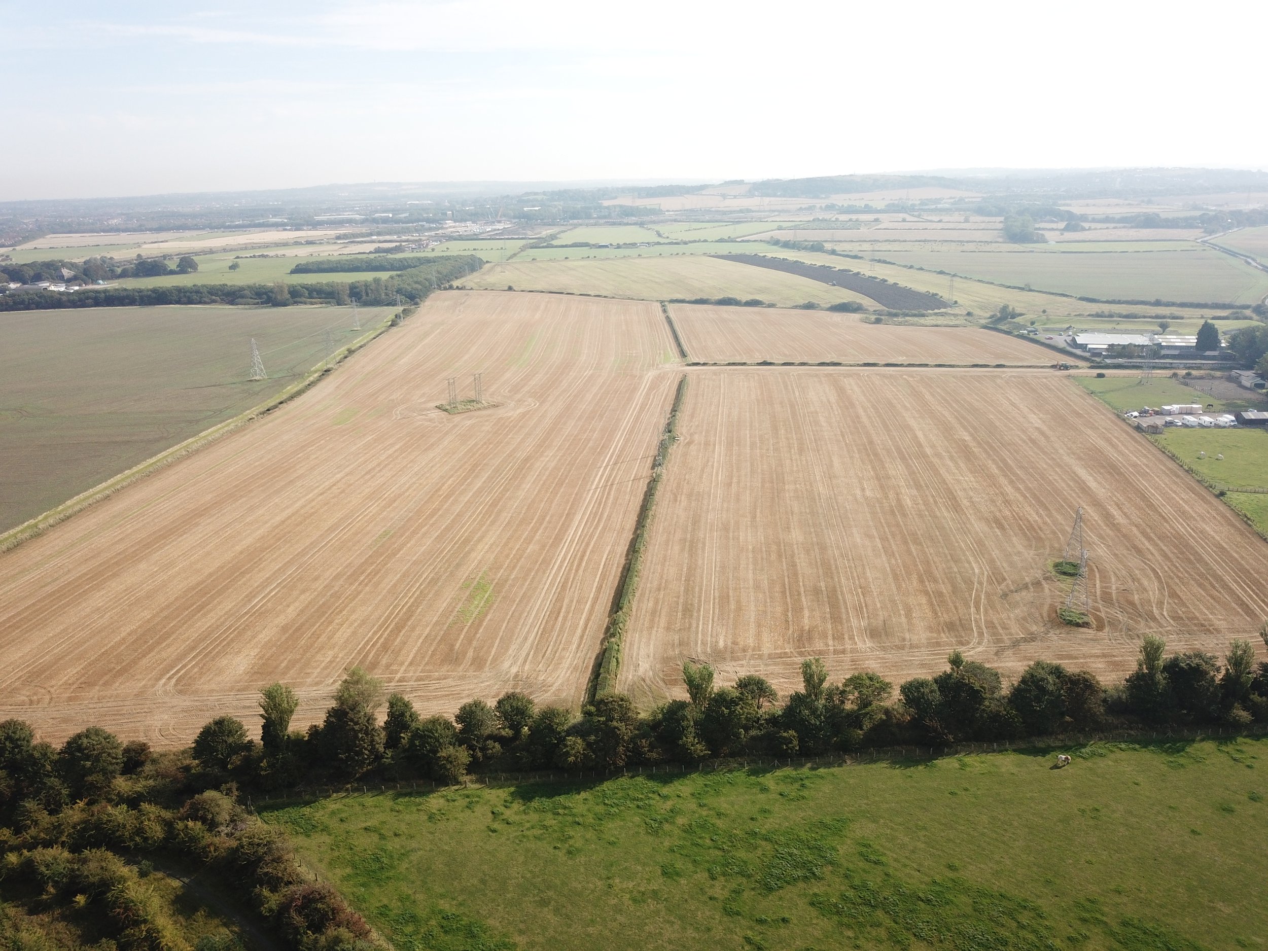 Aerial view of large agricultural fields with power lines and scattered trees, showing a rural landscape under a partly cloudy sky.