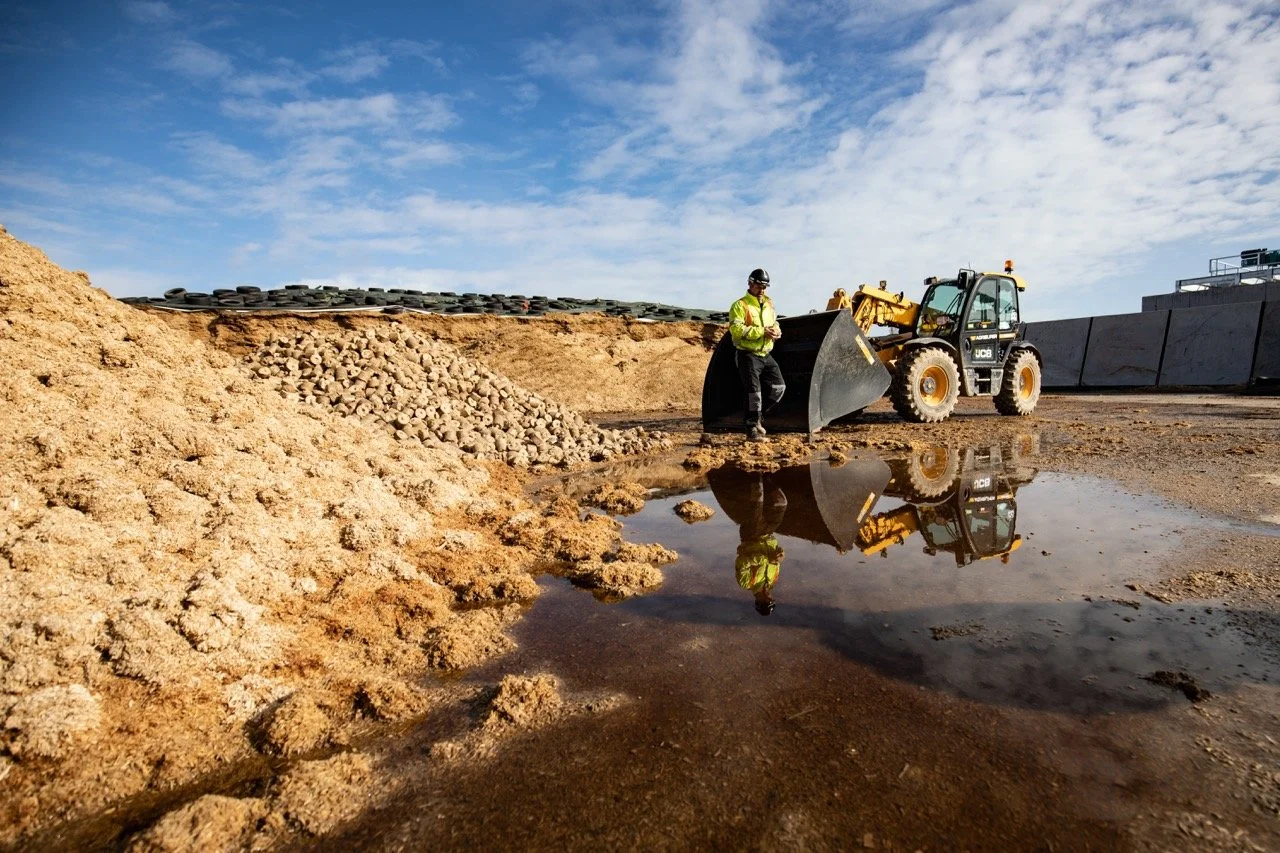 feedstock site with man in high vis jacket, JCB in background, clear blue sky