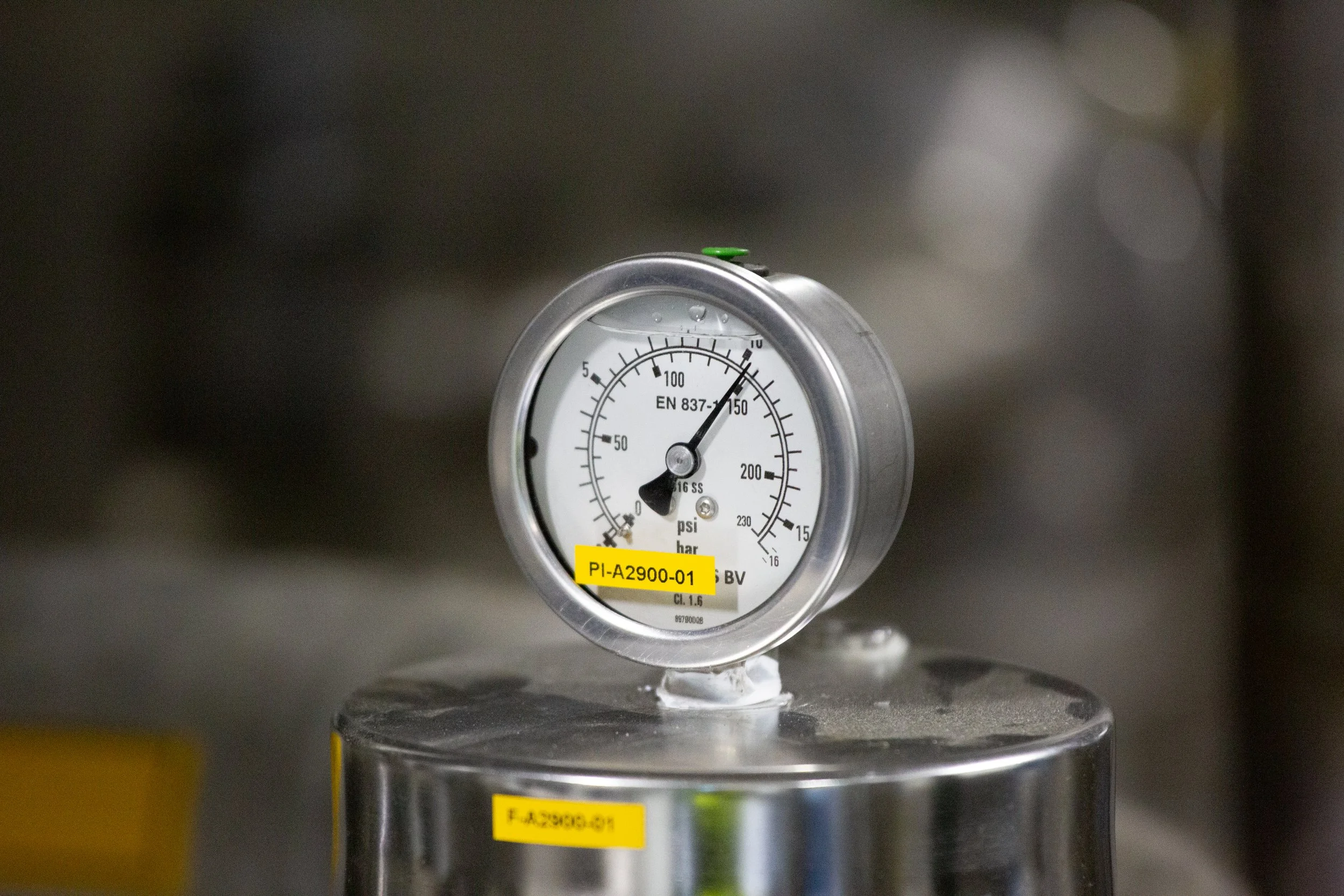 Pressure gauge mounted on stainless steel equipment, indicating pressure in PSI and bar.