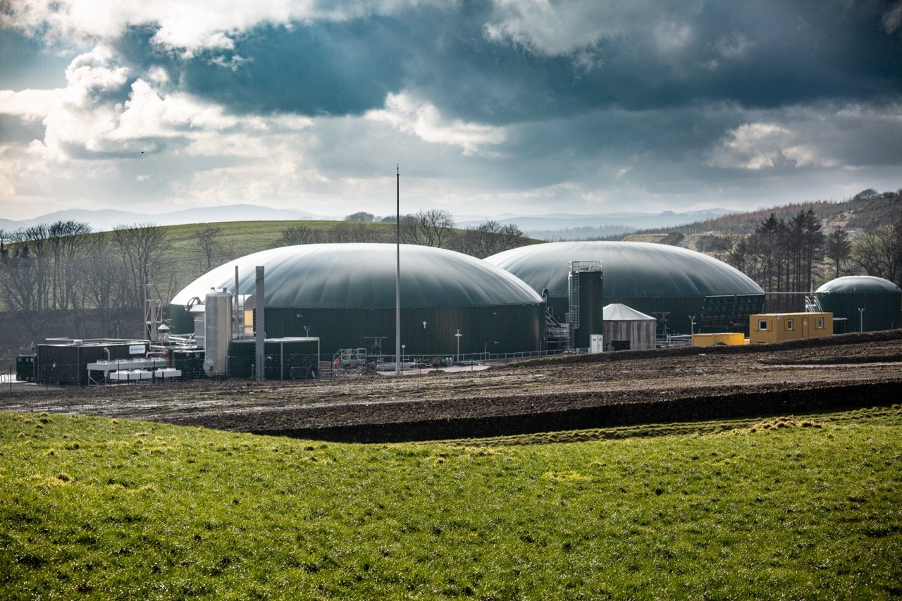 external photograph of biogas plant, hills in background, sunny day