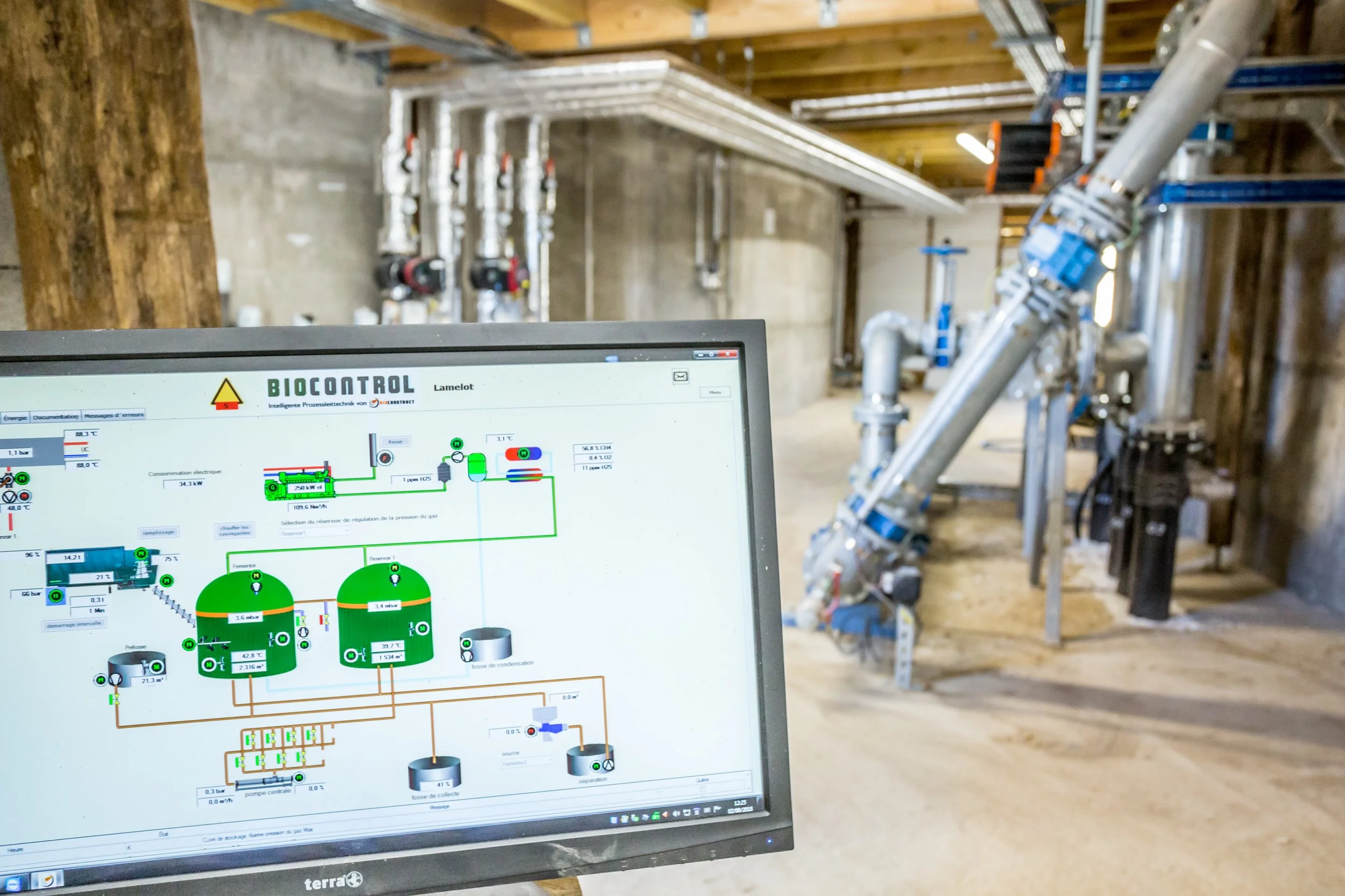 Computer monitor displaying a schematic diagram of an industrial process in a facility with pipes and machinery.