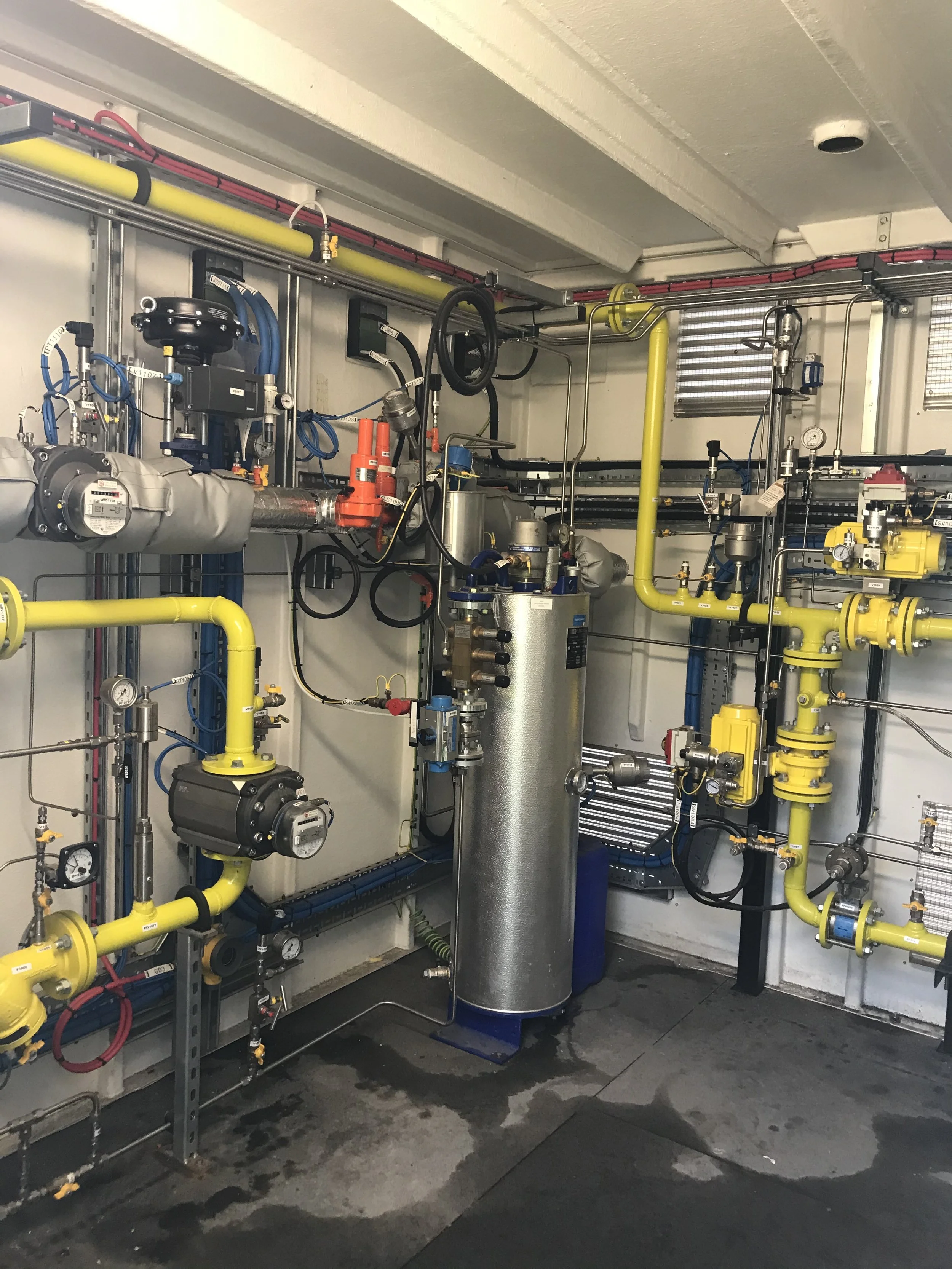 Industrial mechanical room with yellow pipes, gauges, and valves.