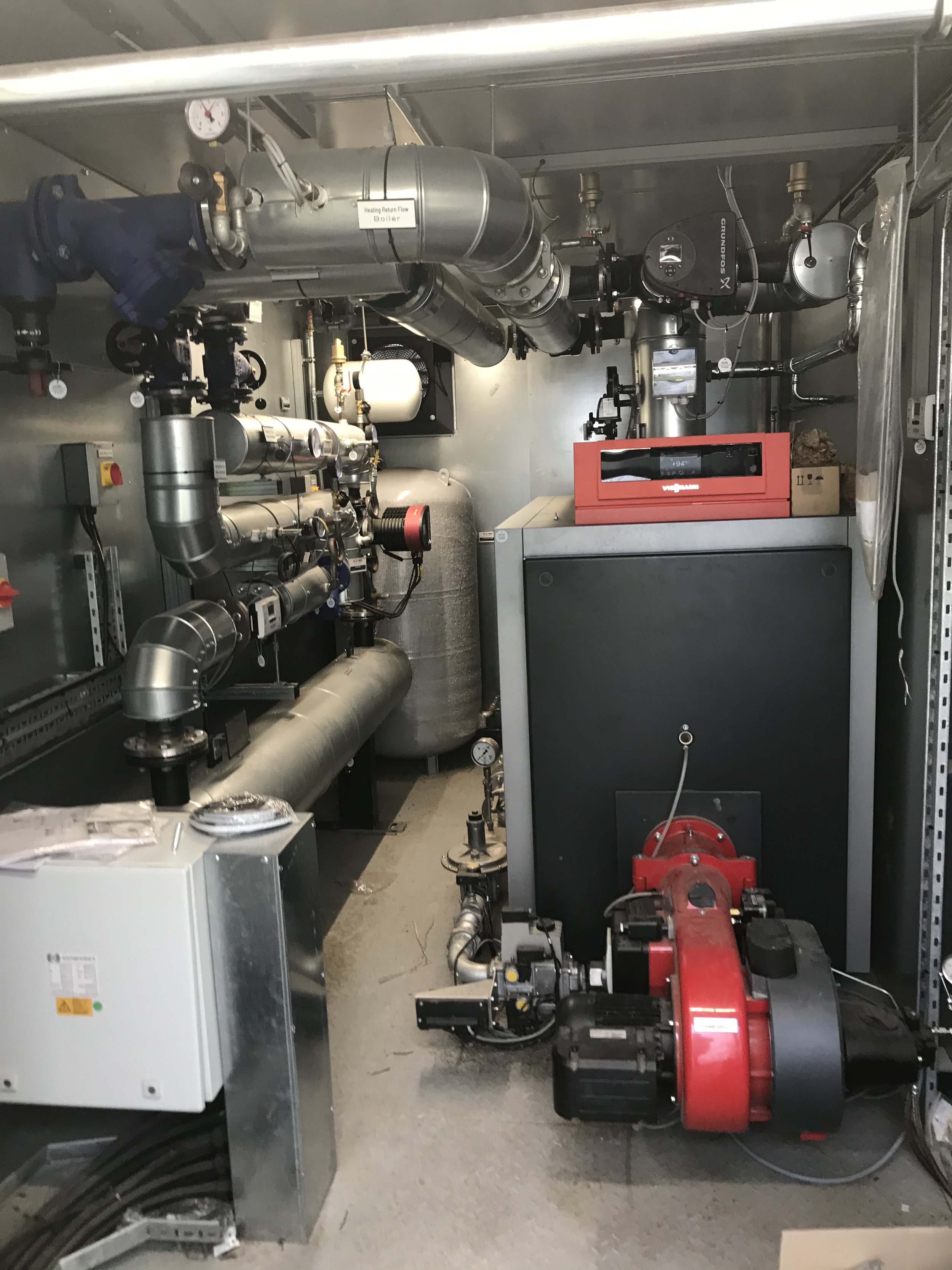 Mechanical room with pipes, gauges, and equipment for heating or industrial processes.