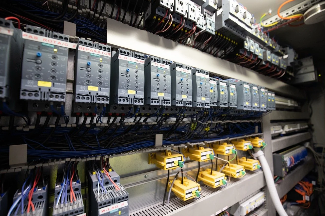 Close-up of electrical control panel with various circuit breakers, wiring, and yellow safety modules.