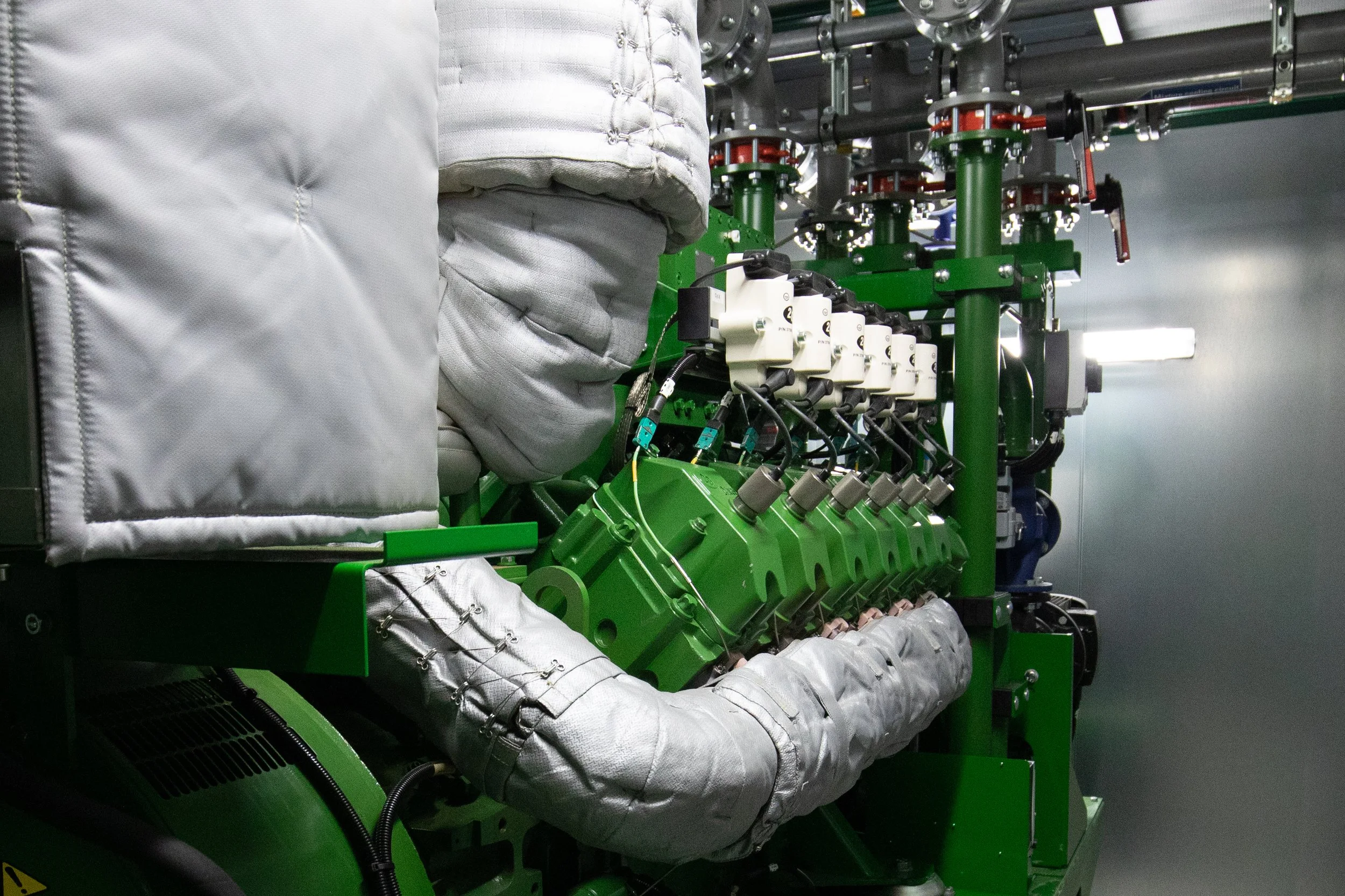 Industrial machinery with green frame and multiple valves, pipes, and insulated components in a controlled environment.