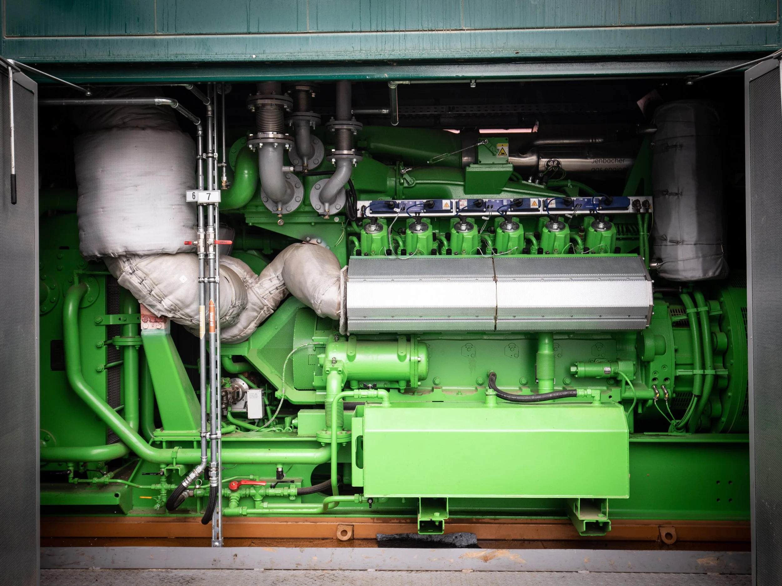 Green industrial engine or generator with various pipes, hoses, and mechanical components.