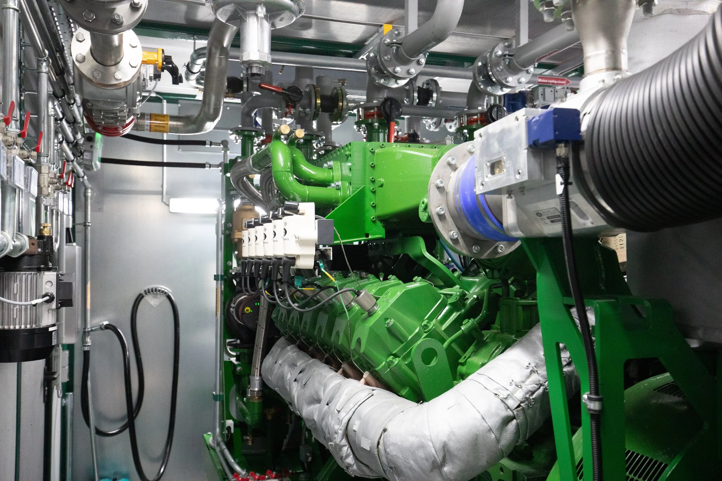 Industrial engine with green-painted components and extensive piping, in a mechanical or manufacturing facility.