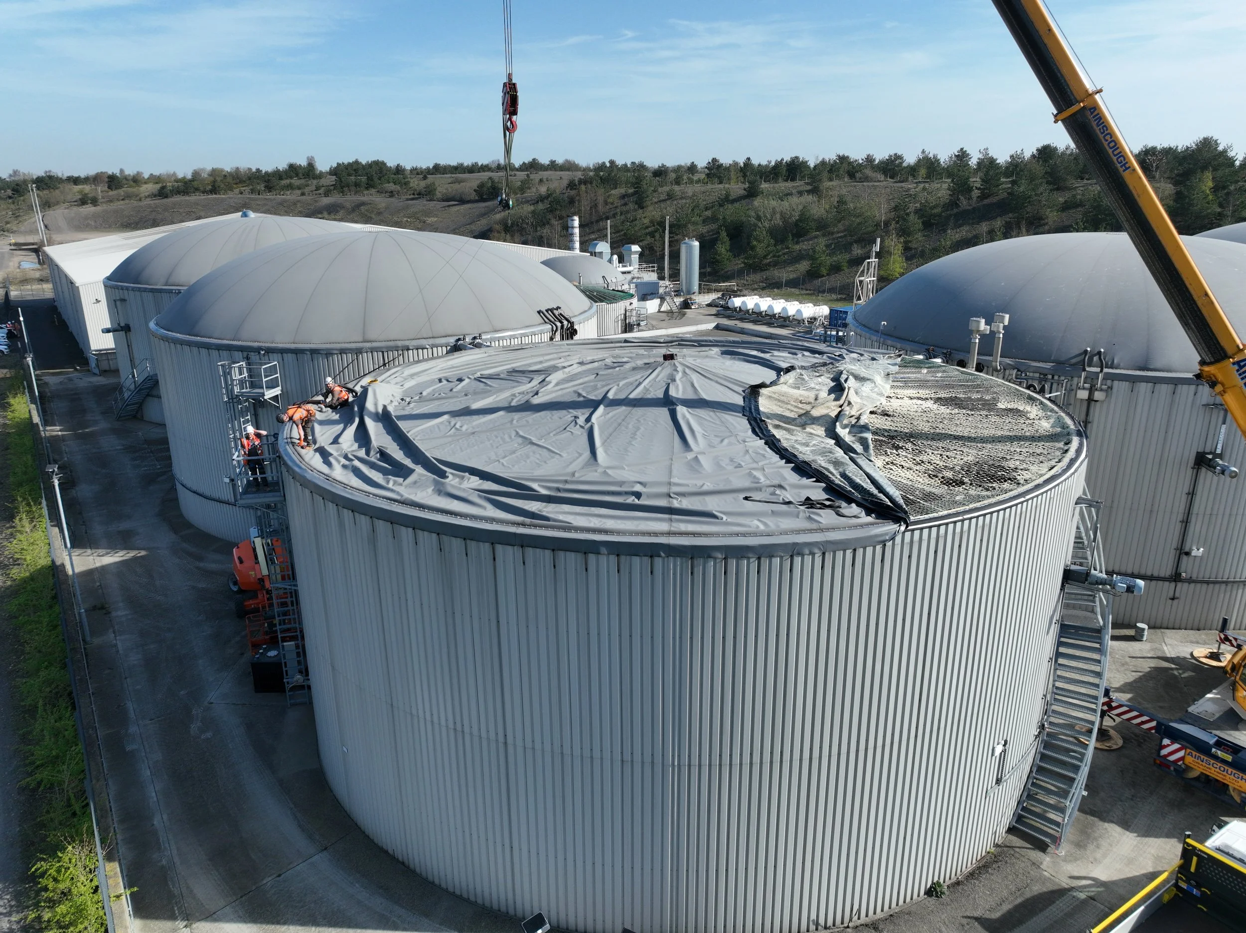 grey tankers with large dome roofs, crane lifting construction workers in orange high vis jackets