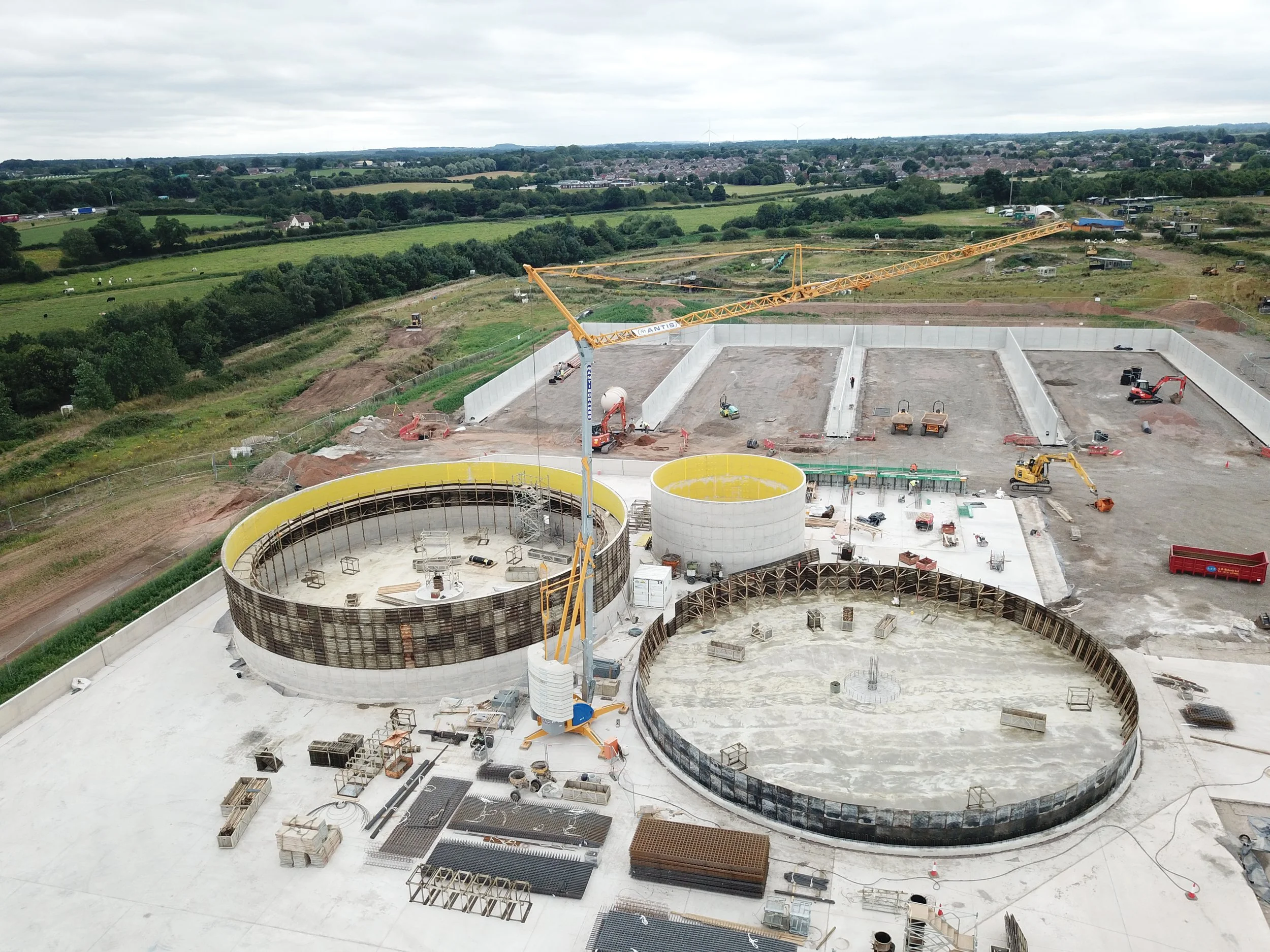 anaerobic digestion plant under construction, large concrete tankers, cranes, surrounded by green fields