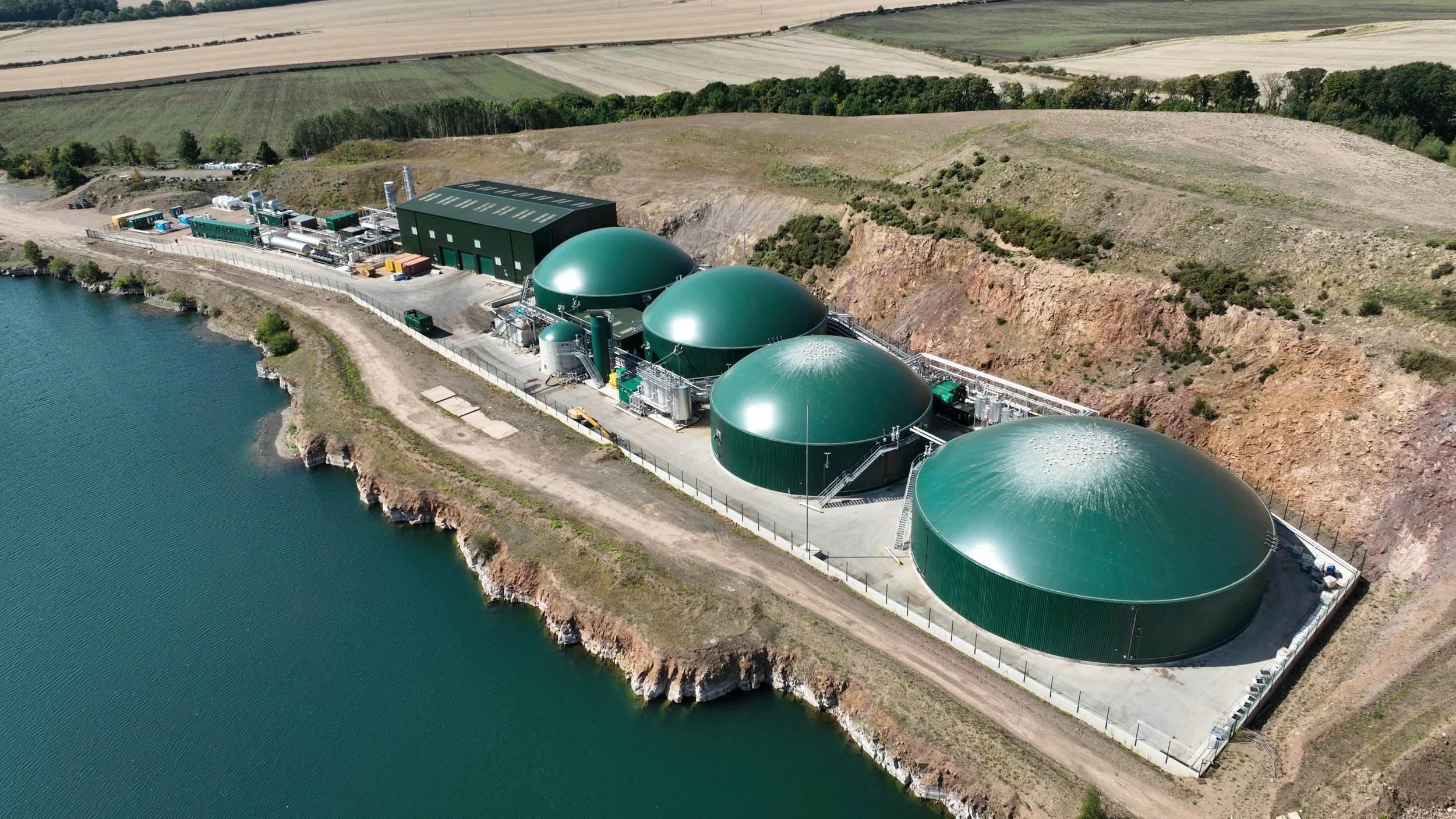 Aerial image of anaerobic digestion plant, next to lake, green fields, large green containers