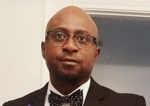A man in a tuxedo with a polka dot bow tie and glasses, posing for a photo indoors.