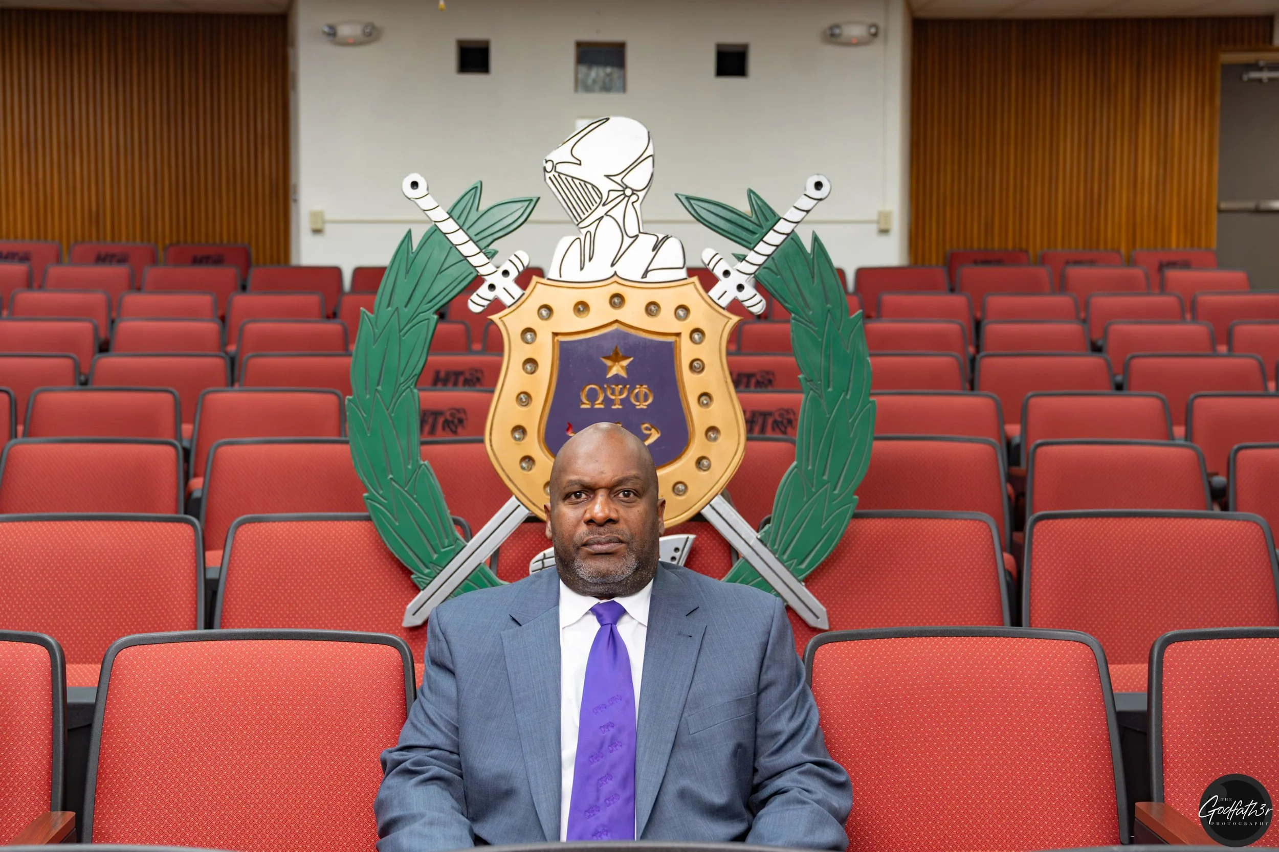 Black and white portrait of a man wearing glasses, a checkered shirt, and a suit jacket.