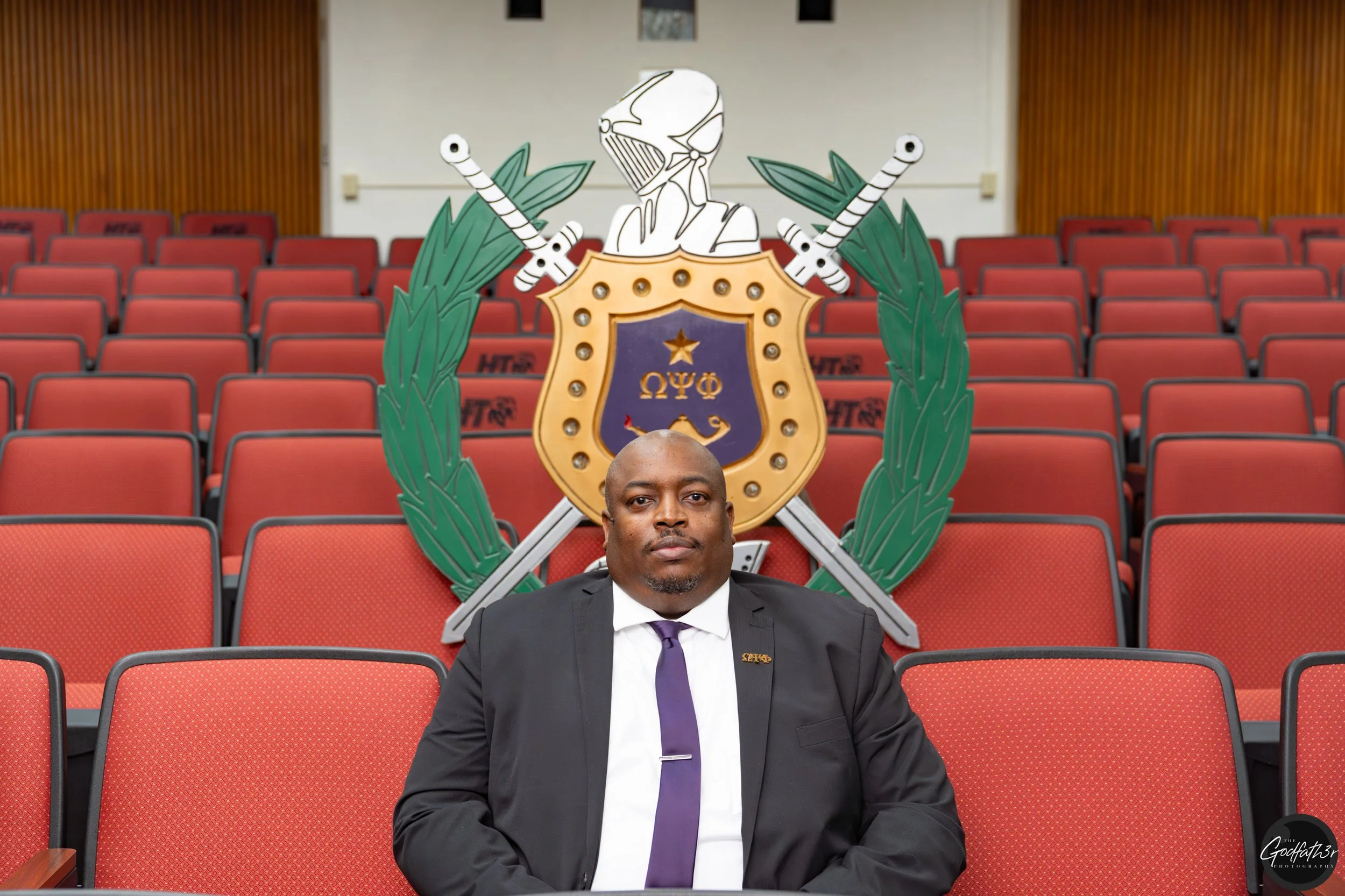 A smiling man with short hair, dark skin, wearing a light-colored suit and patterned tie.