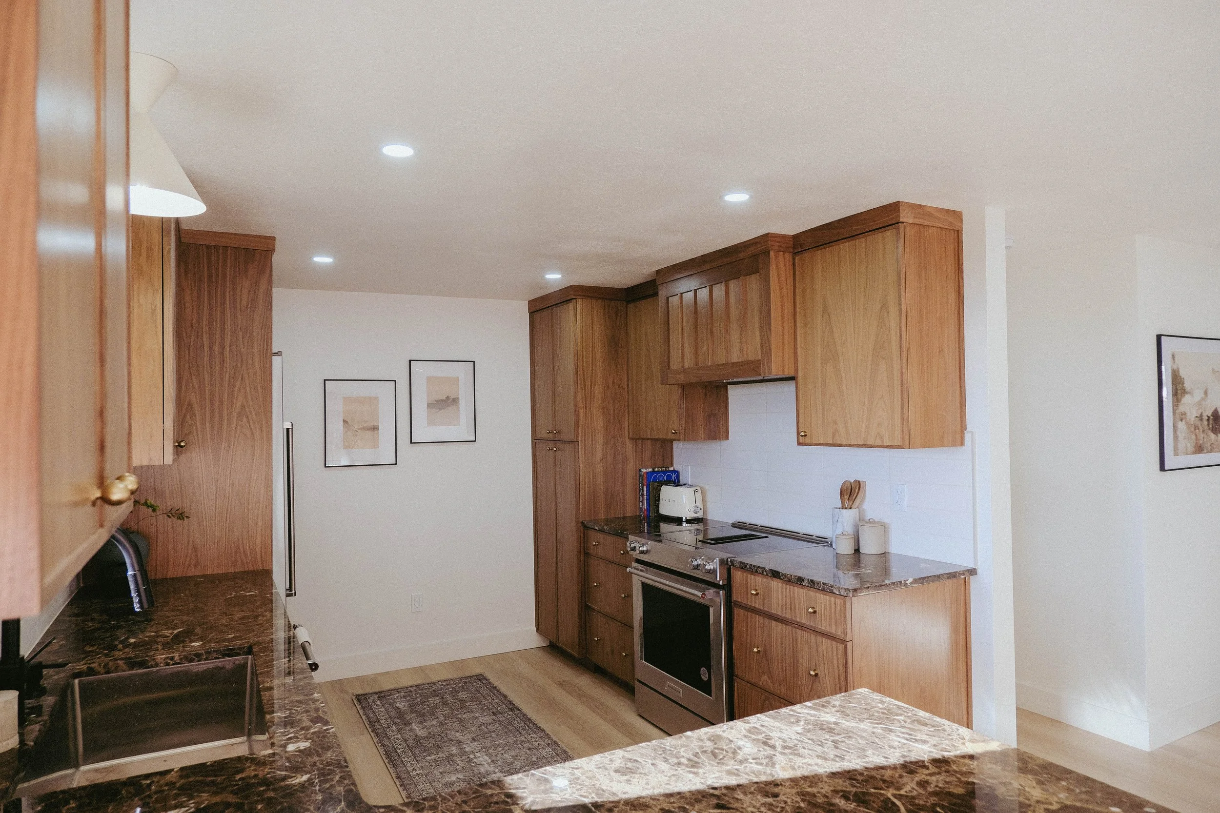 A kitchen with wooden cabinets, a black marble countertop, a stainless steel oven, and framed artwork on white walls.