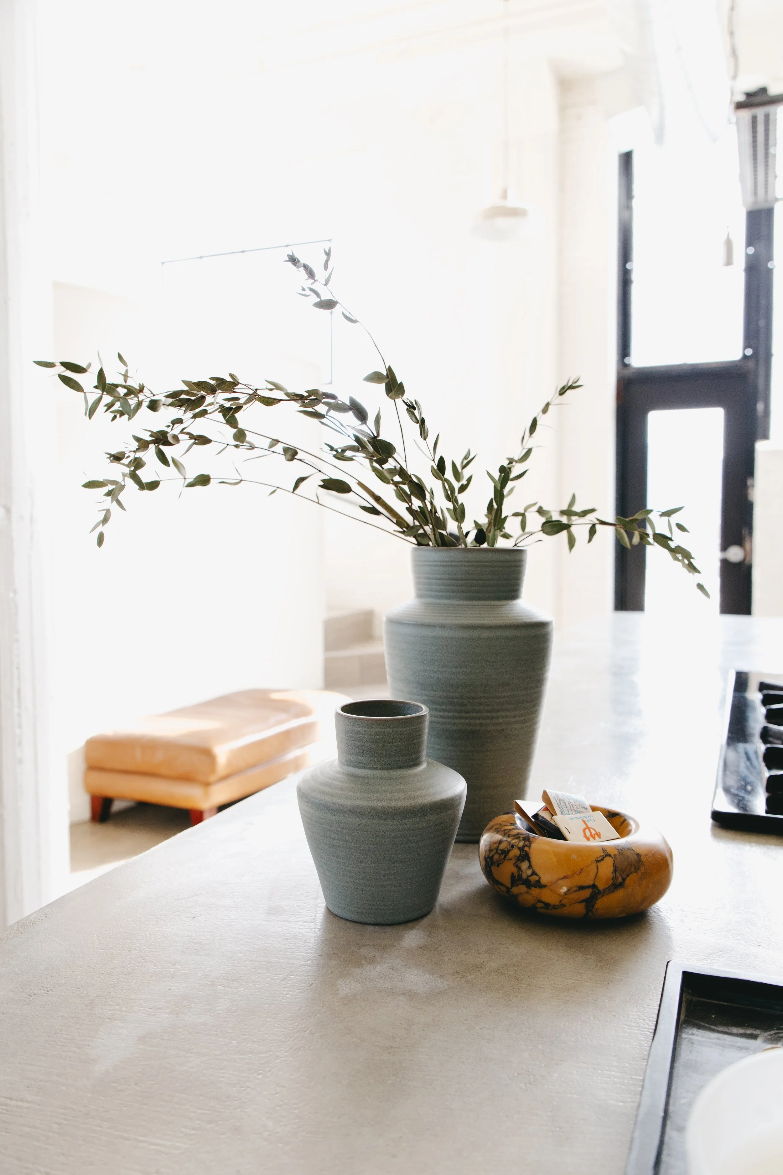 Staging services by Riley James Interiors in Salt Lake City, Utah. A kitchen countertop with two vases, one large with green leafy branches and one small, and a decorative marble bowl with tea bags.