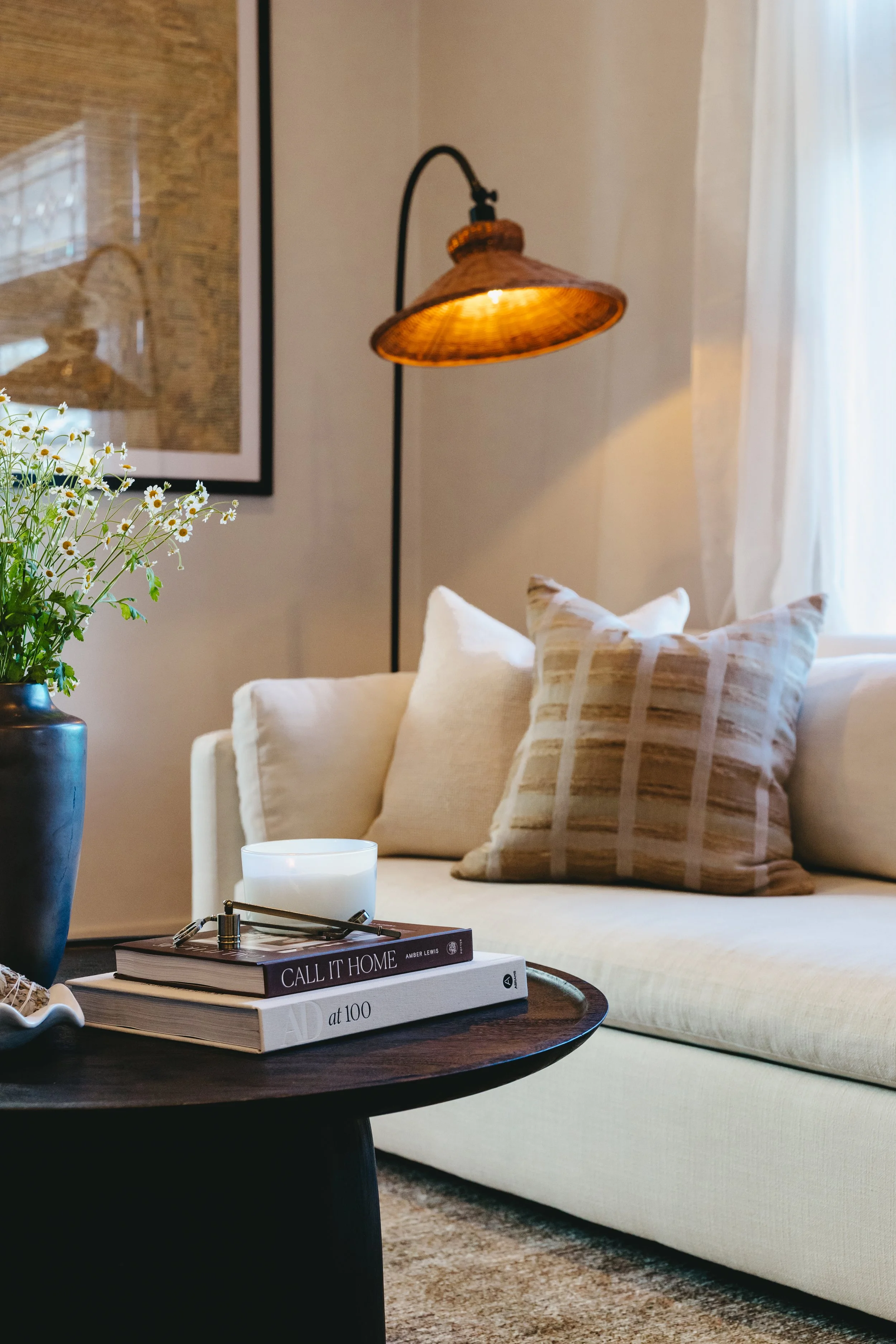Cozy staged living room in a vacant Salt Lake City home featuring a white sofa with neutral beige cushions, a warm wood coffee table styled with books and a candle, fresh florals in a vase, and a soft ambient pendant light. Professionally staged.