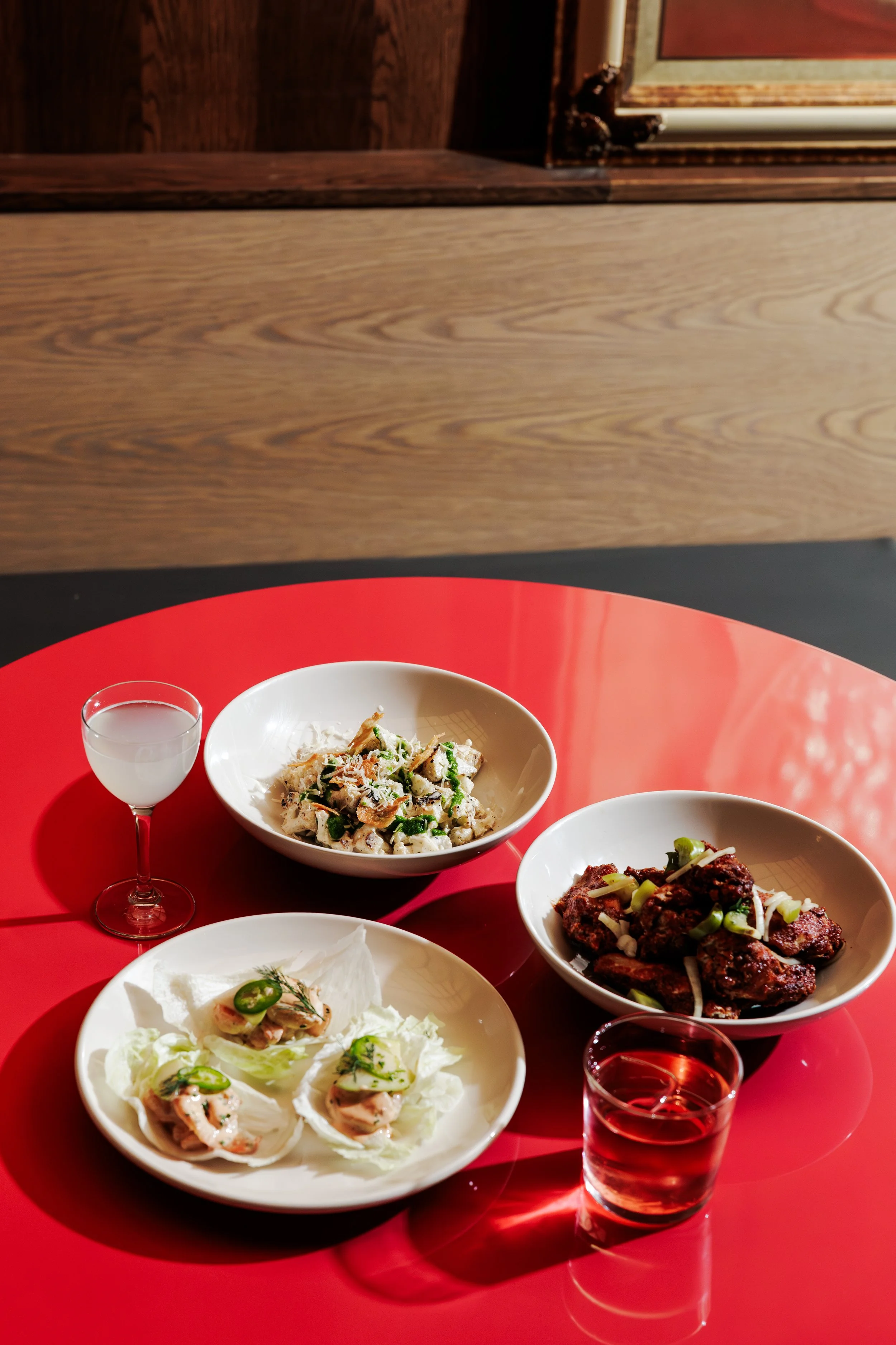 A red round table with three bowls of food and two glasses of drinks, featuring appetizers and dishes on a red table.