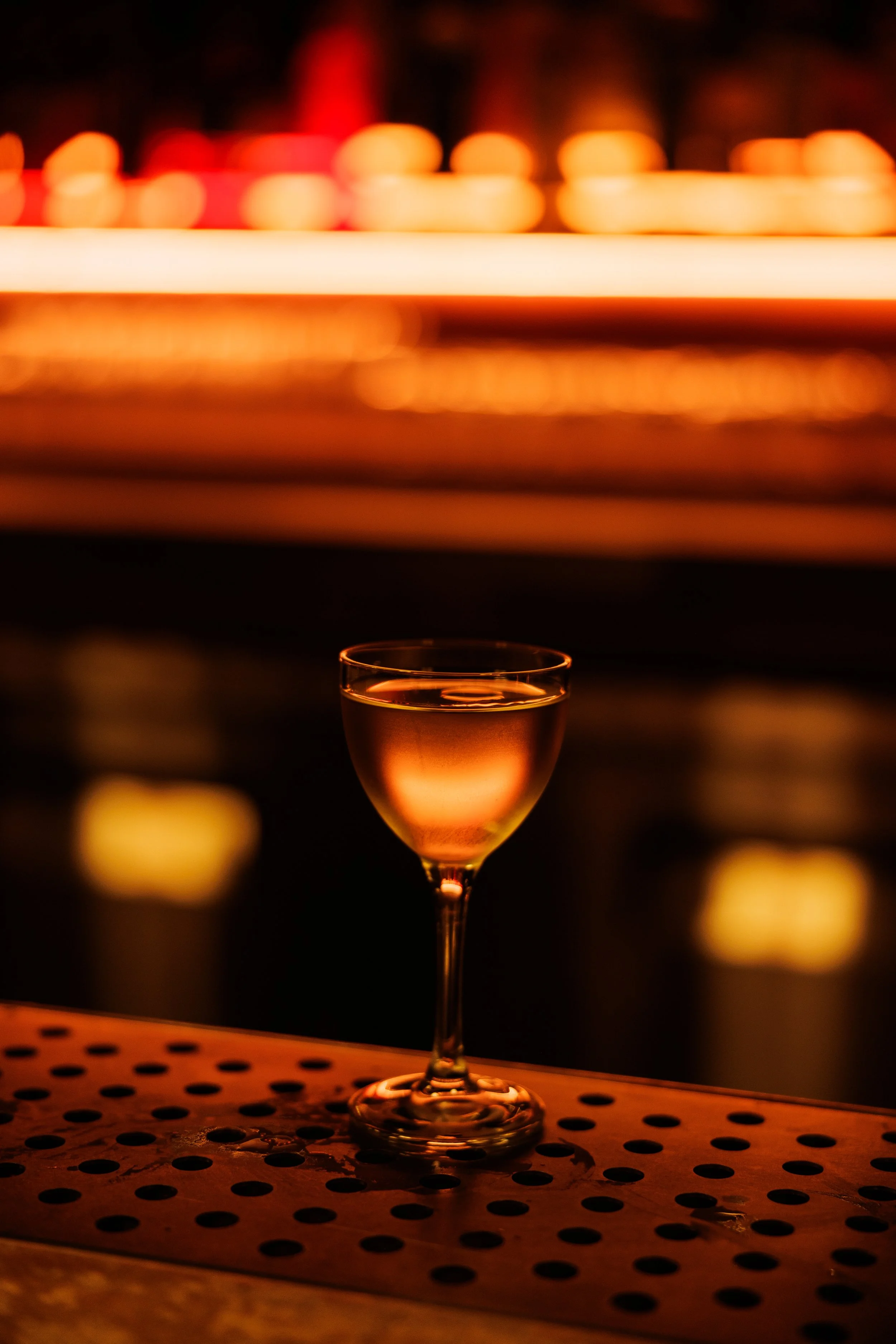 A glass of rosé wine on a bar surface with blurred colorful lights in the background.