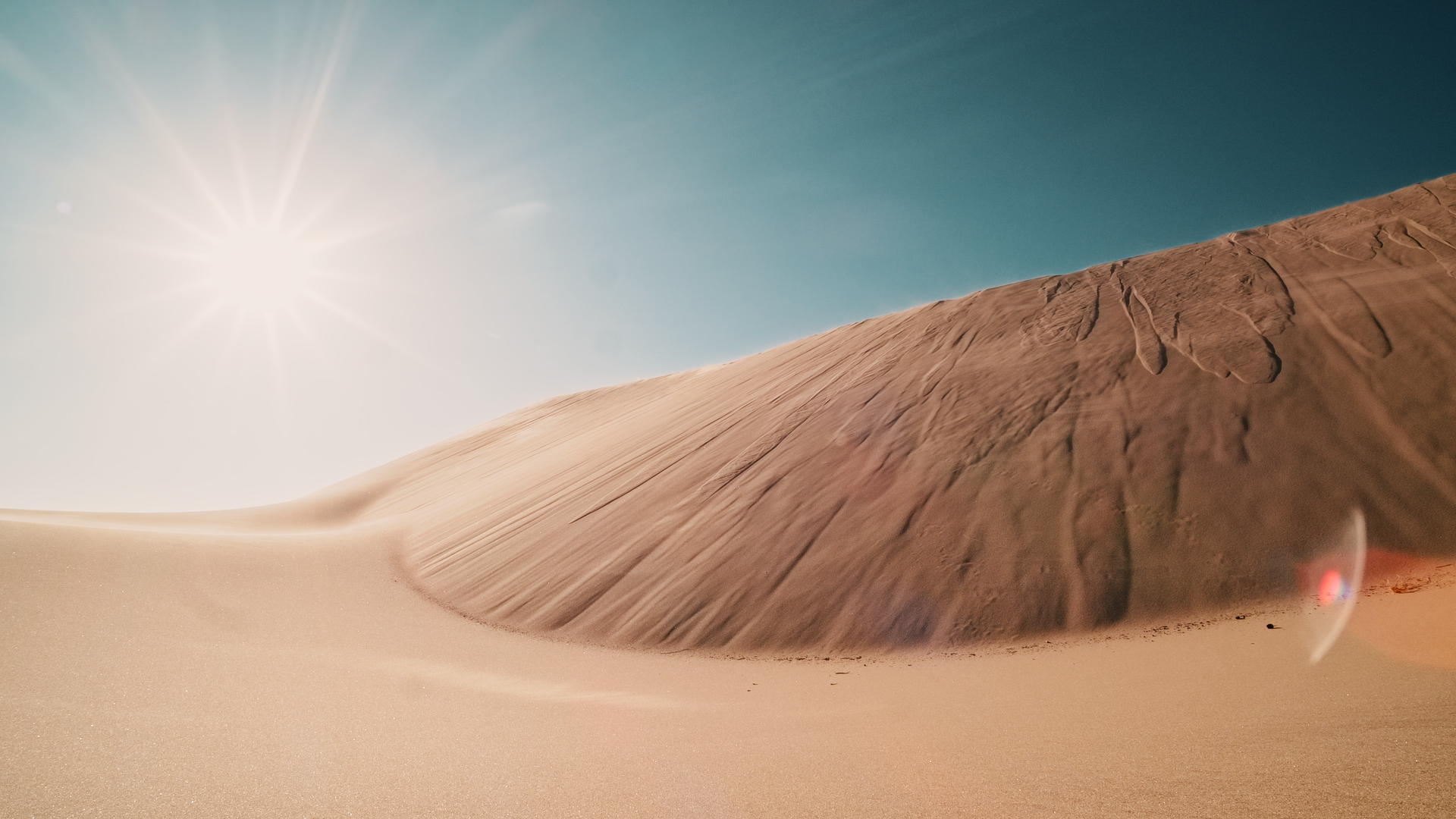 A desert with sand dunes and a bright sun in the sky.