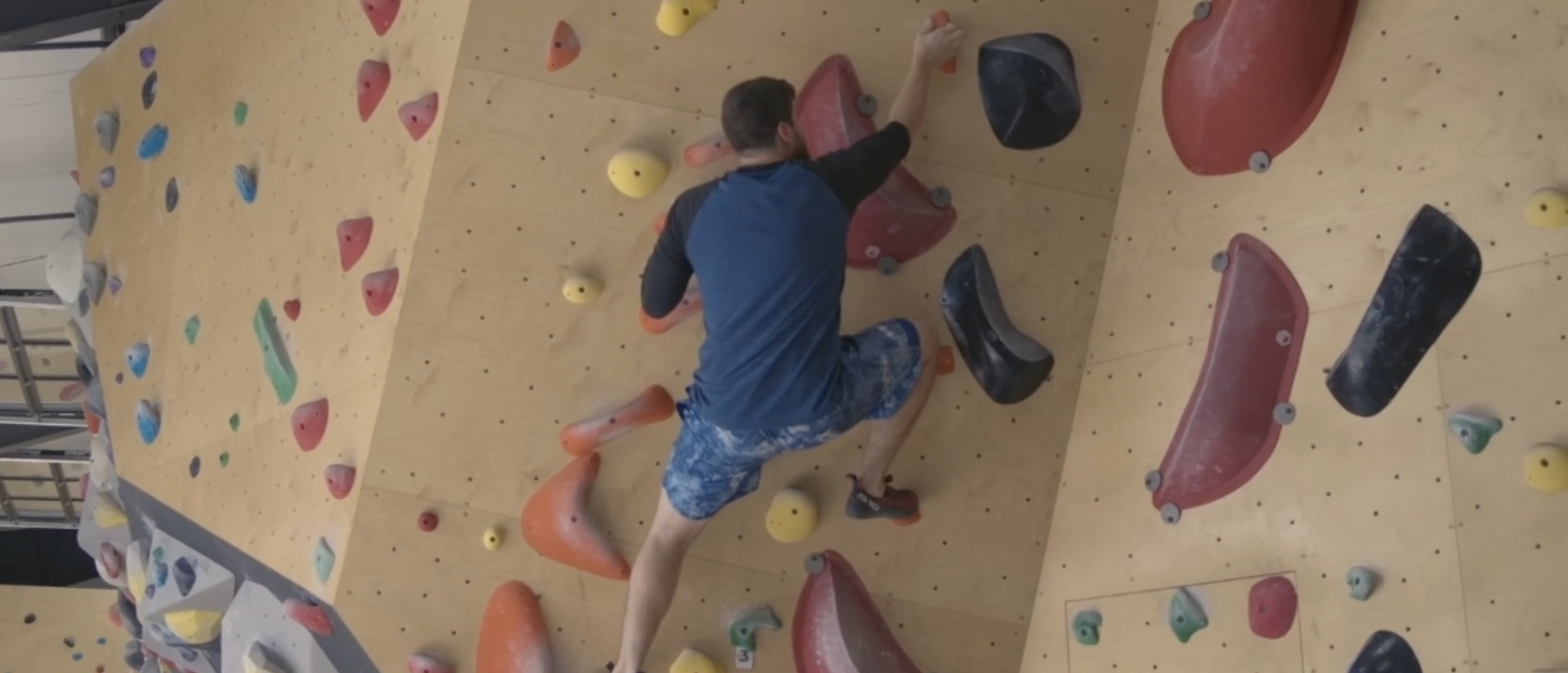 An individual climbing an indoor rock climbing wall with colorful holds.