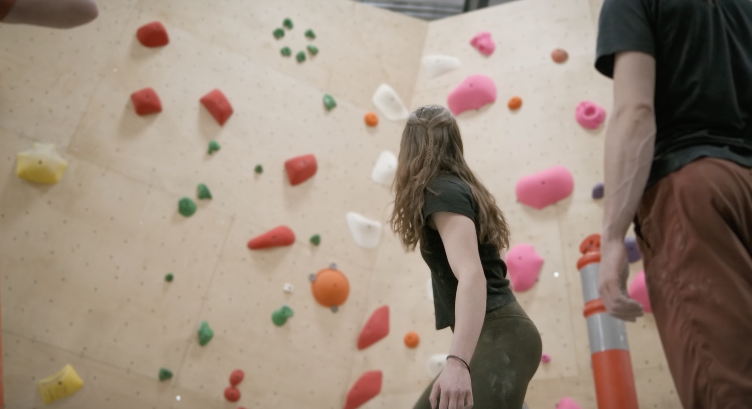 People climbing on an indoor rock climbing wall with colorful holds.