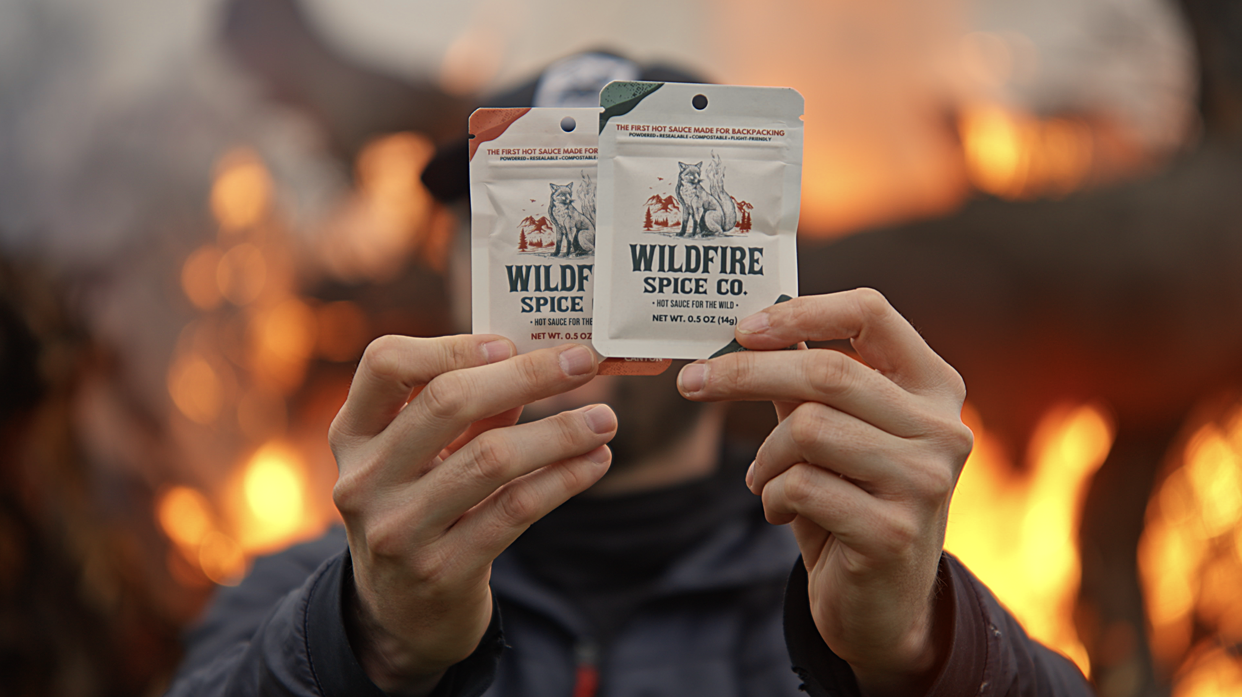 Person holding two small packets of wildfire spice with a forest fire in the background