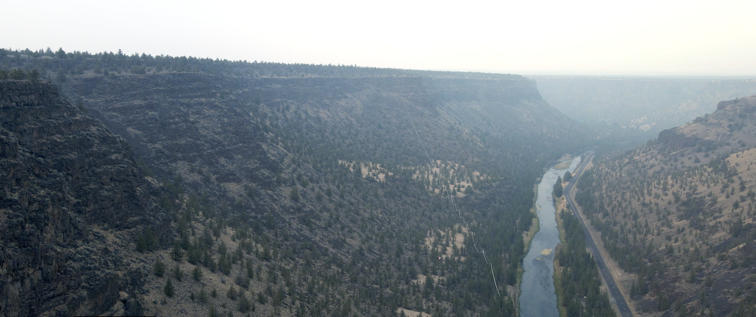 Aerial view of a canyon with steep cliffs, a winding river at the bottom, and a road running parallel to the river on the right side.