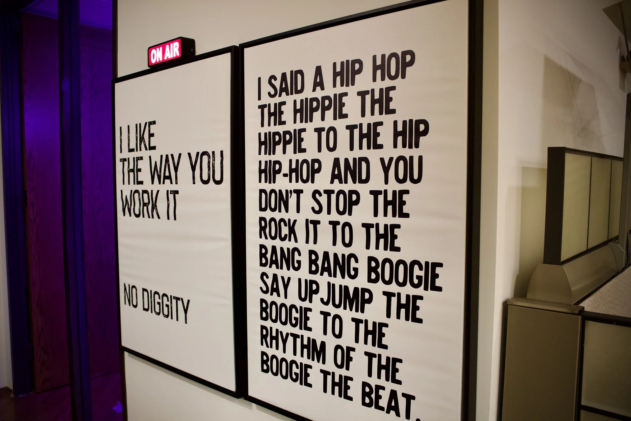 Two large white boards with black text of song lyrics, with a red and white 'On Air' sign above them.