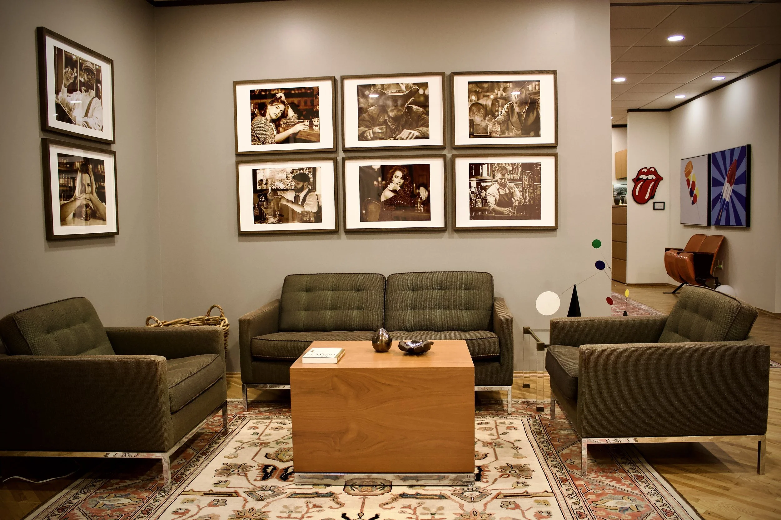 A cozy TV lounge area with a central wooden coffee table, three green upholstered chairs, a light rug, and framed black-and-white photographs on the walls.