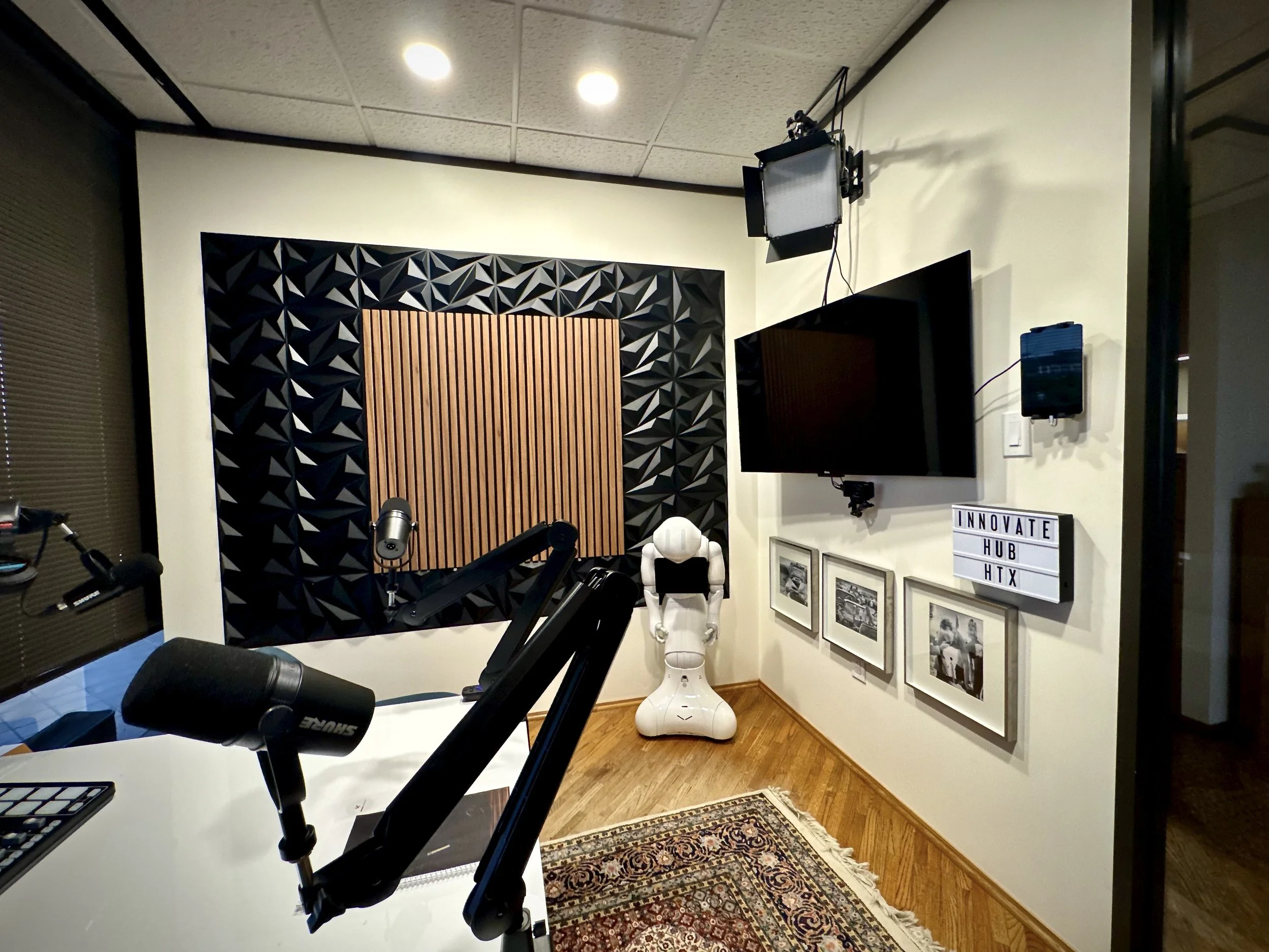Recording studio with panels, a large flat-screen TV, framed photos, a robot, and a sign reading 'Innovate Hub HTX'.